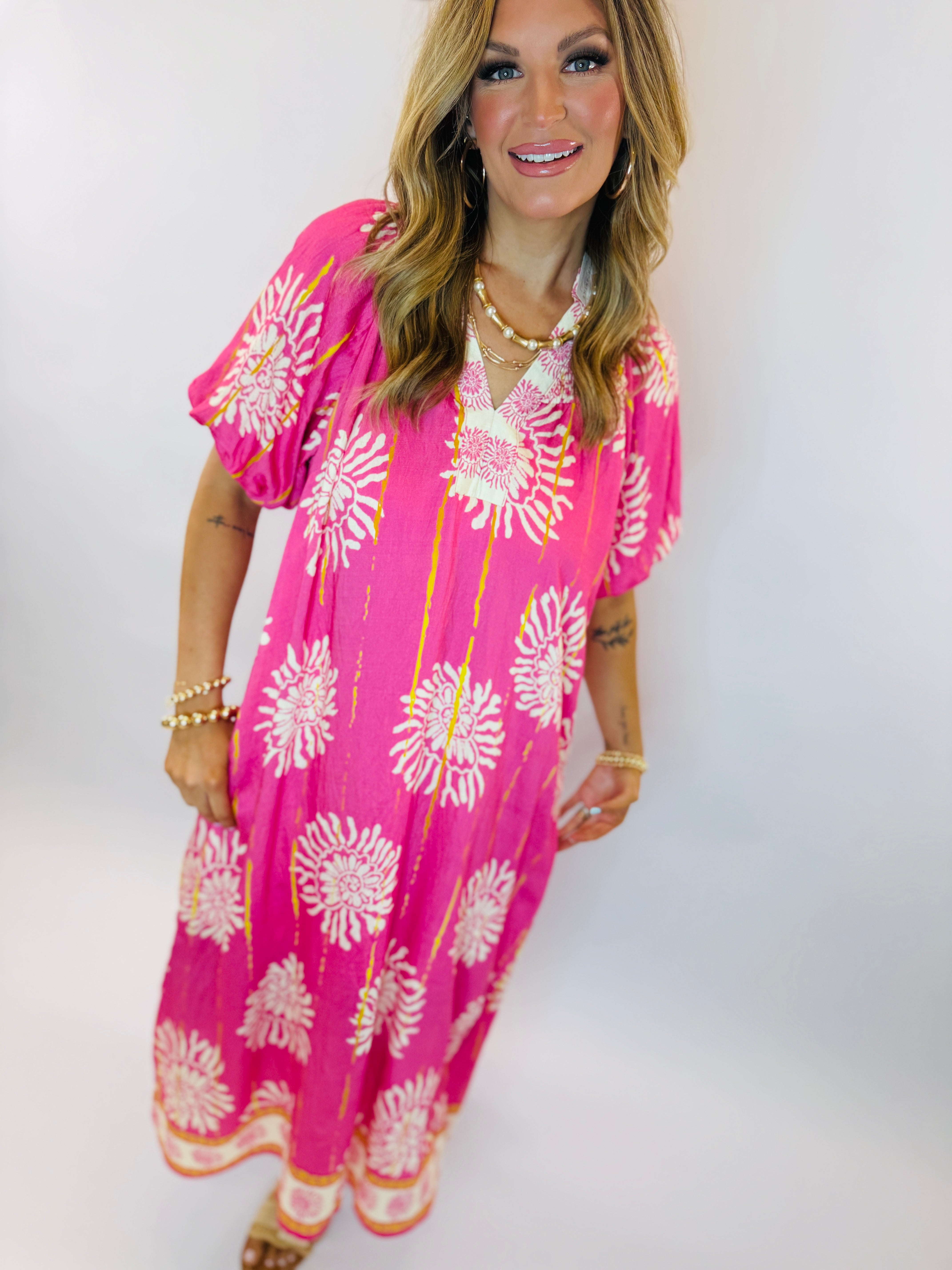 Woman wearing bright pink floral maxi dress with white and yellow sunburst pattern and short sleeves