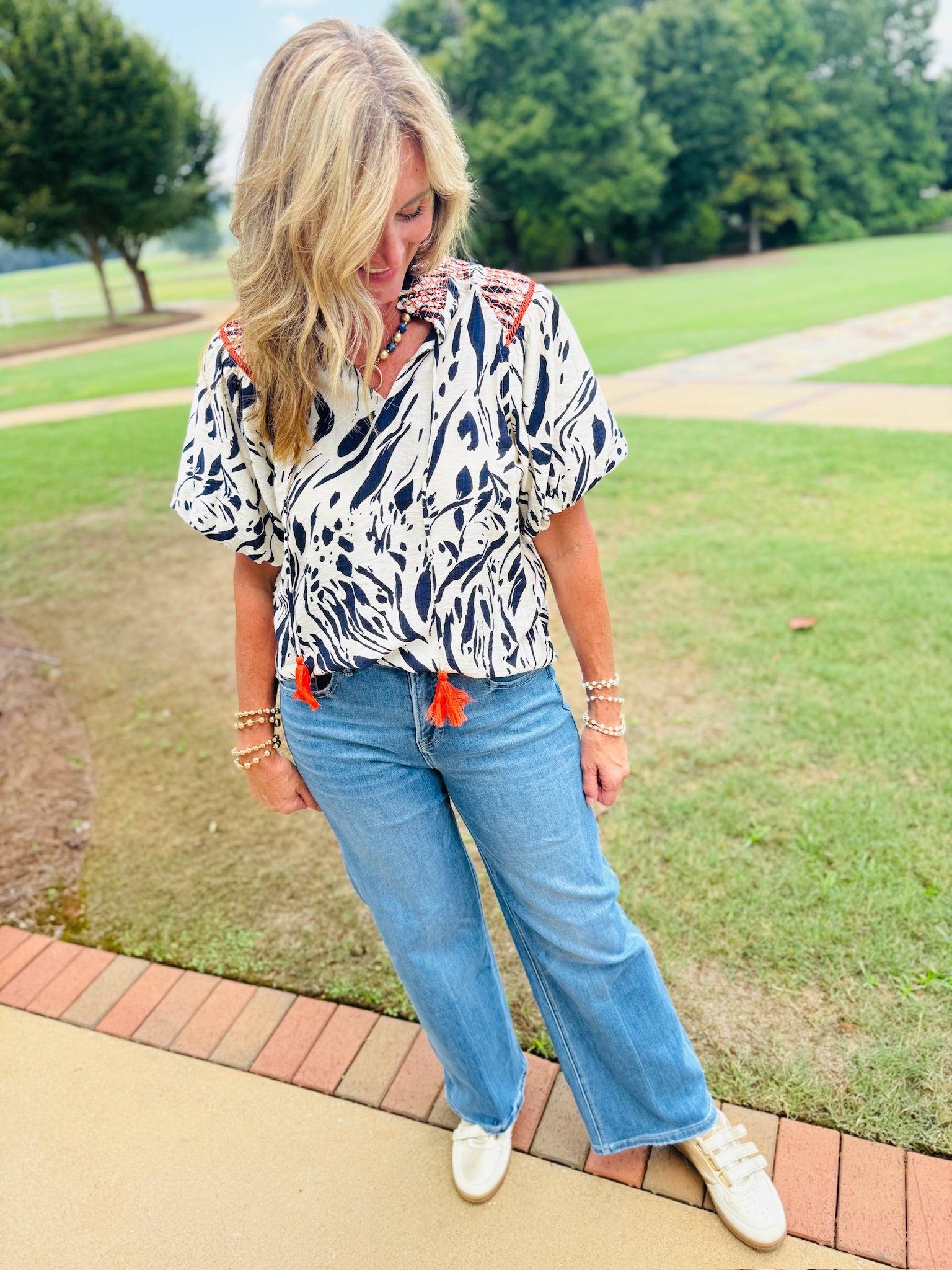 Woman wearing Rita Top in navy and white abstract print with orange tassels, paired with light wash jeans.
