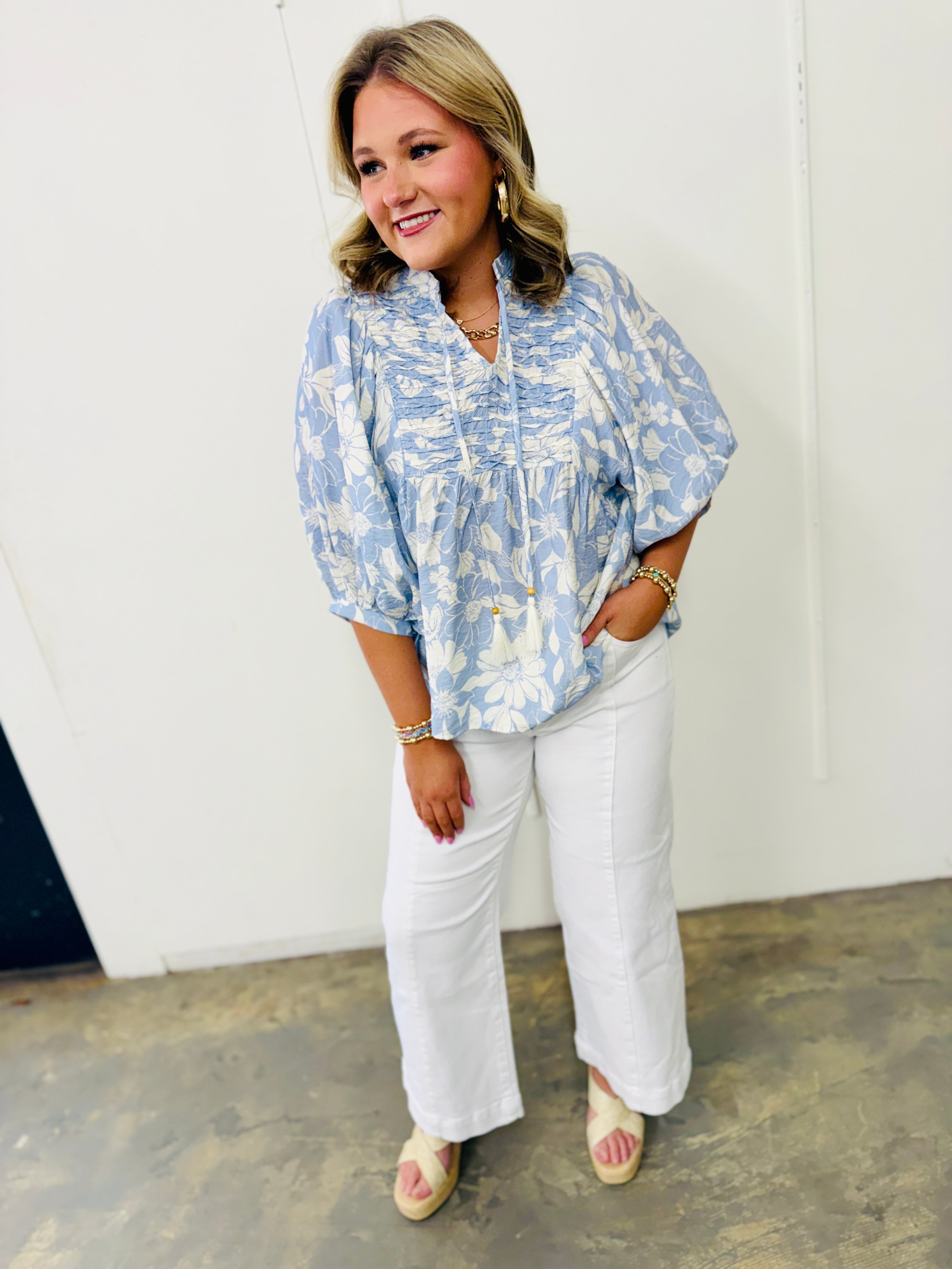 Woman wearing blue and white floral Alaya Soft Top with white pants and platform sandals