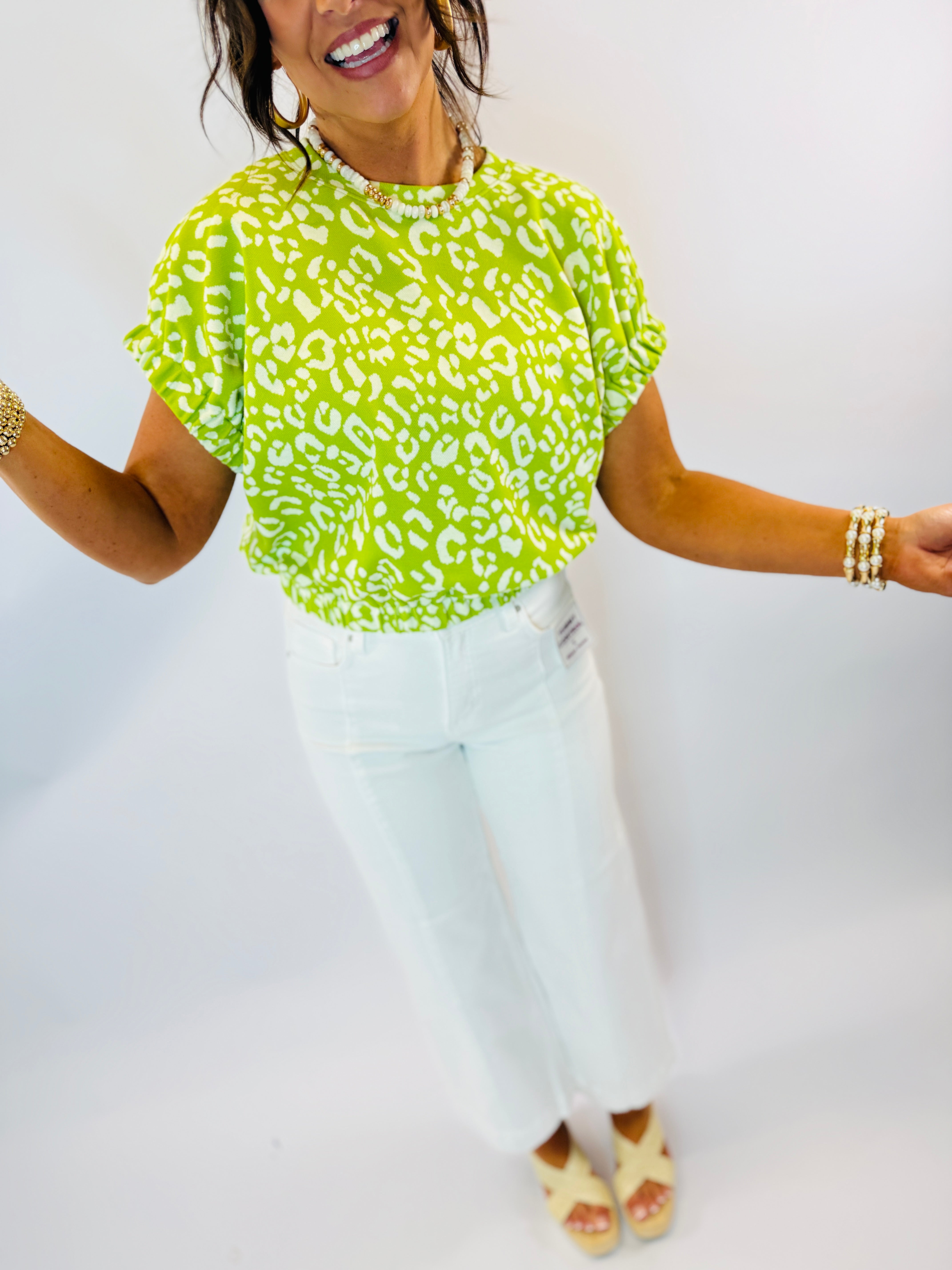 Woman wearing bright green leopard print Tally Top with white jeans and gold accessories
