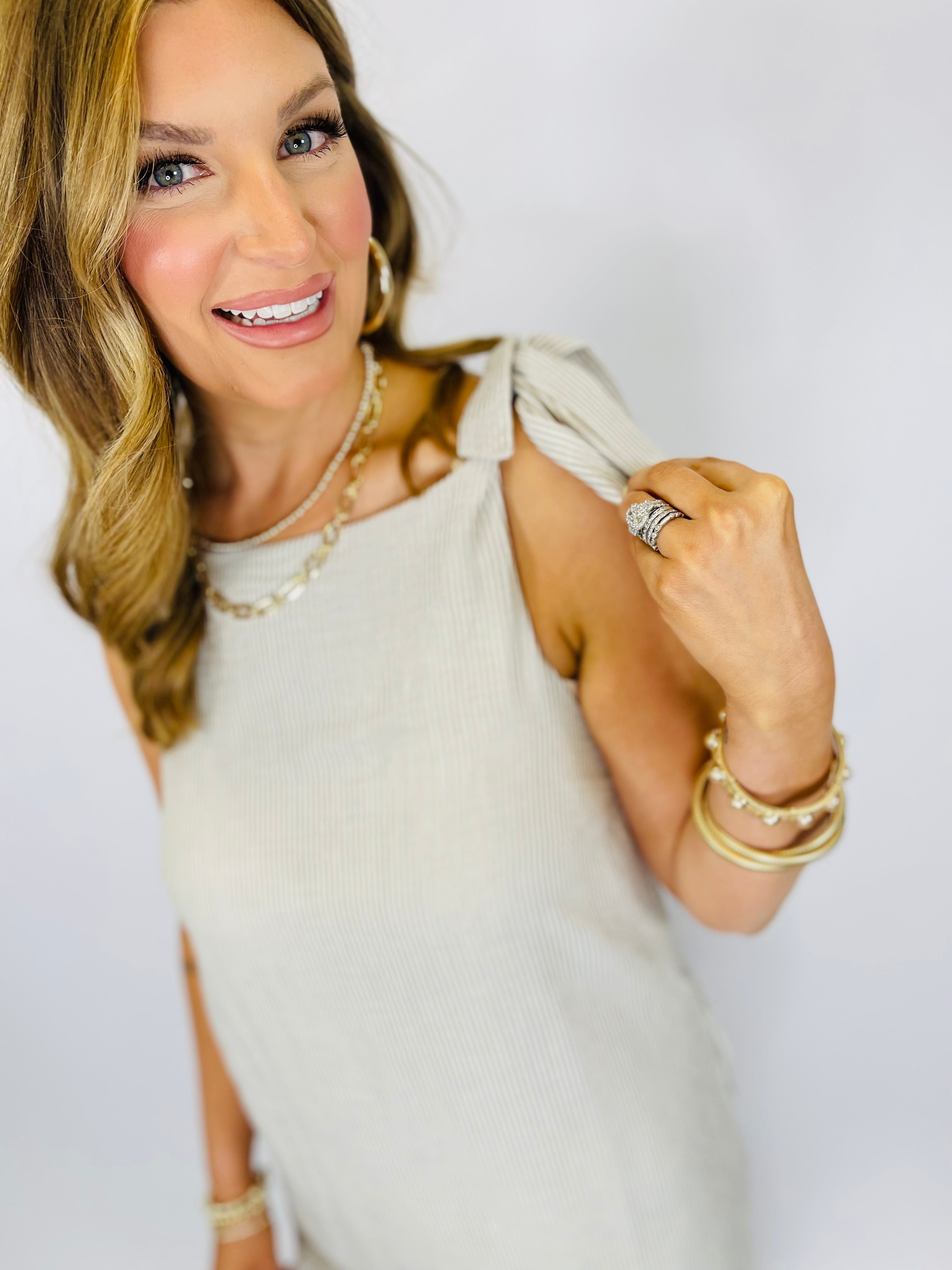 Woman wearing cream-colored sleeveless Alexis dress with gold jewelry and bracelets, smiling at camera.
