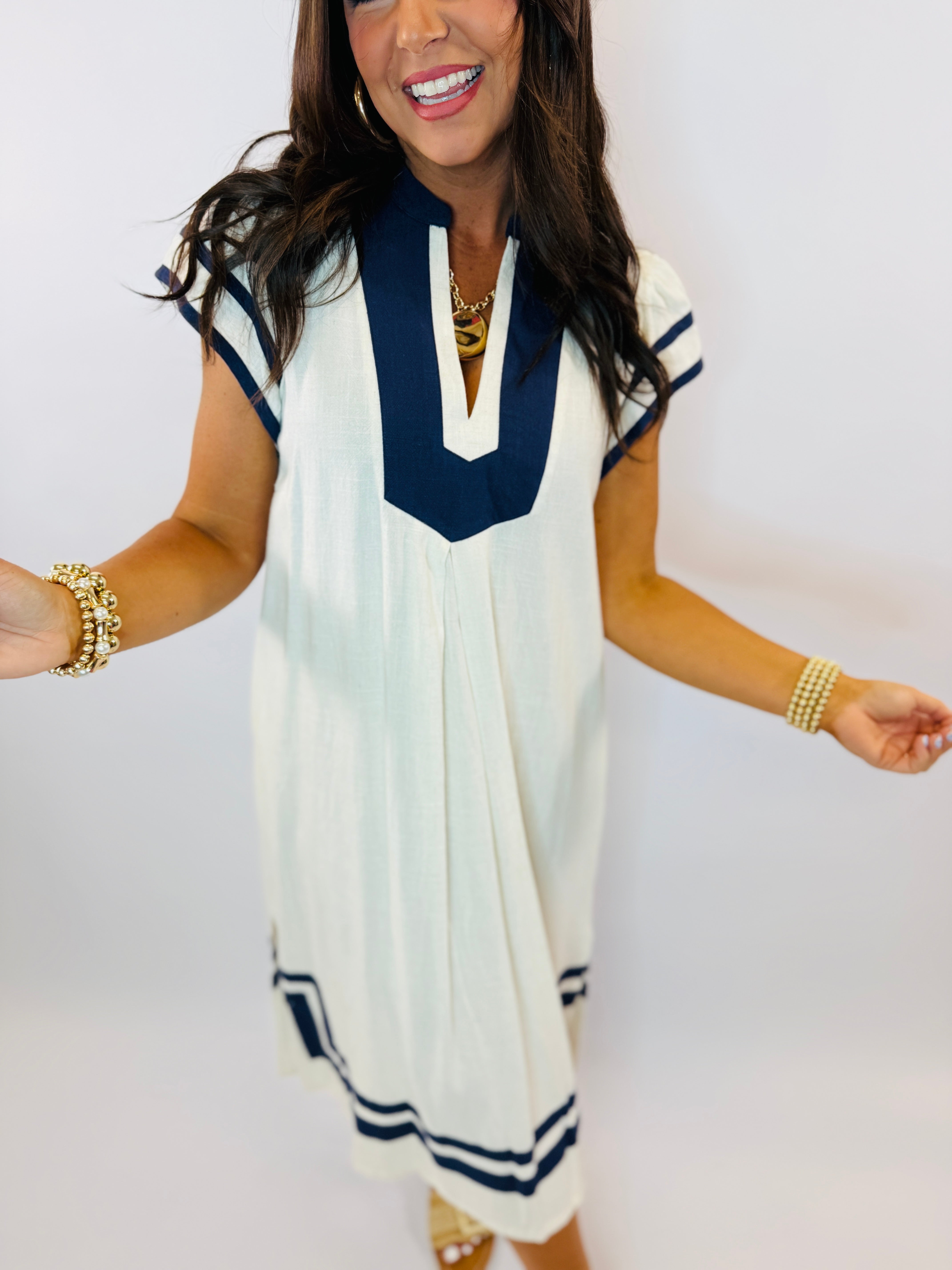 Woman wearing white midi dress with navy blue trim and cap sleeves, styled with gold jewelry
