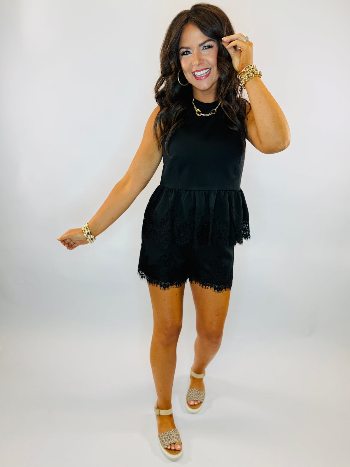Woman wearing black sleeveless lace-trimmed peplum top with gold jewelry and platform sandals