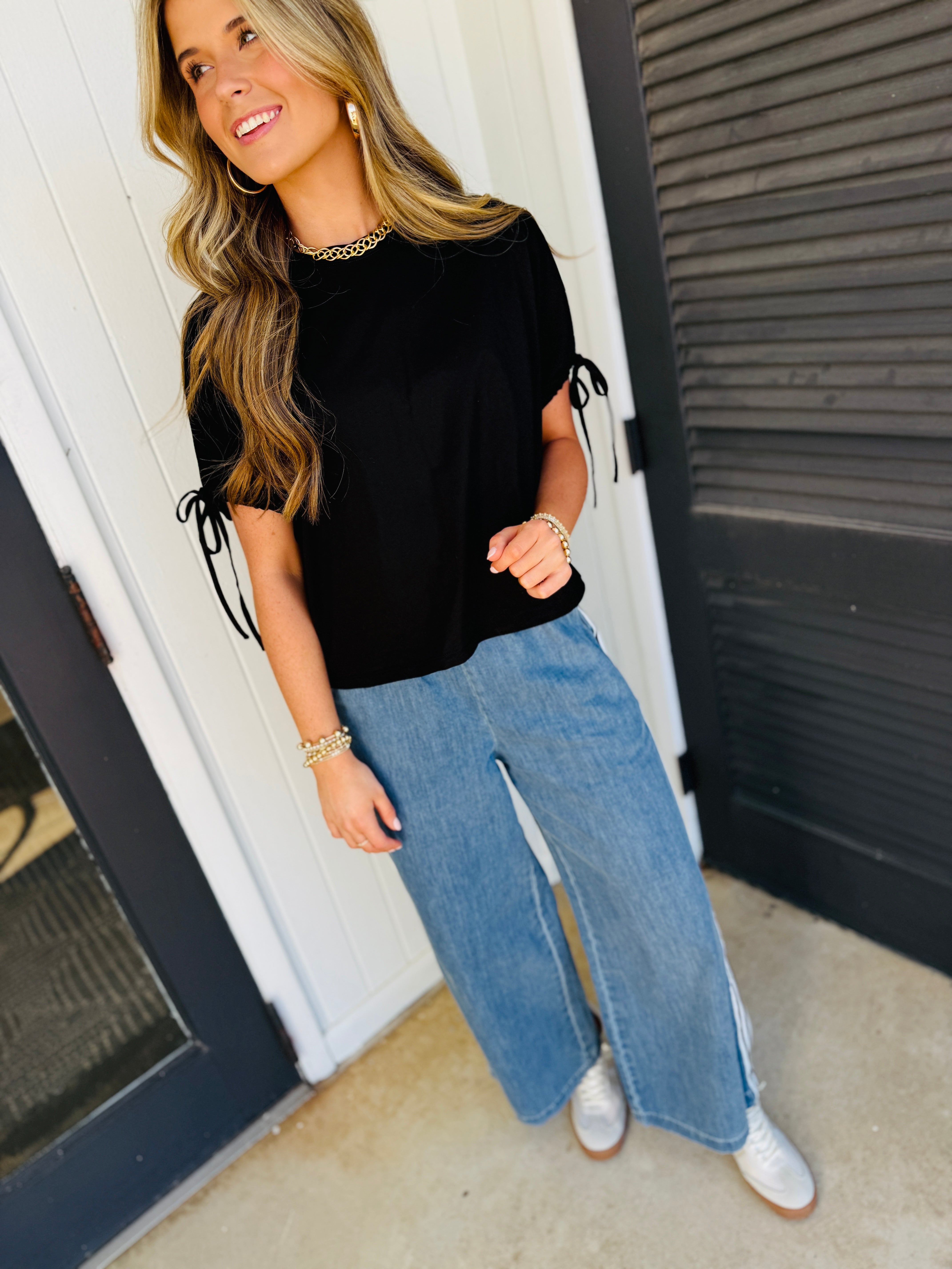 Woman wearing Ayah Willow relaxed blue wide-leg pants with black top and gold jewelry accessories