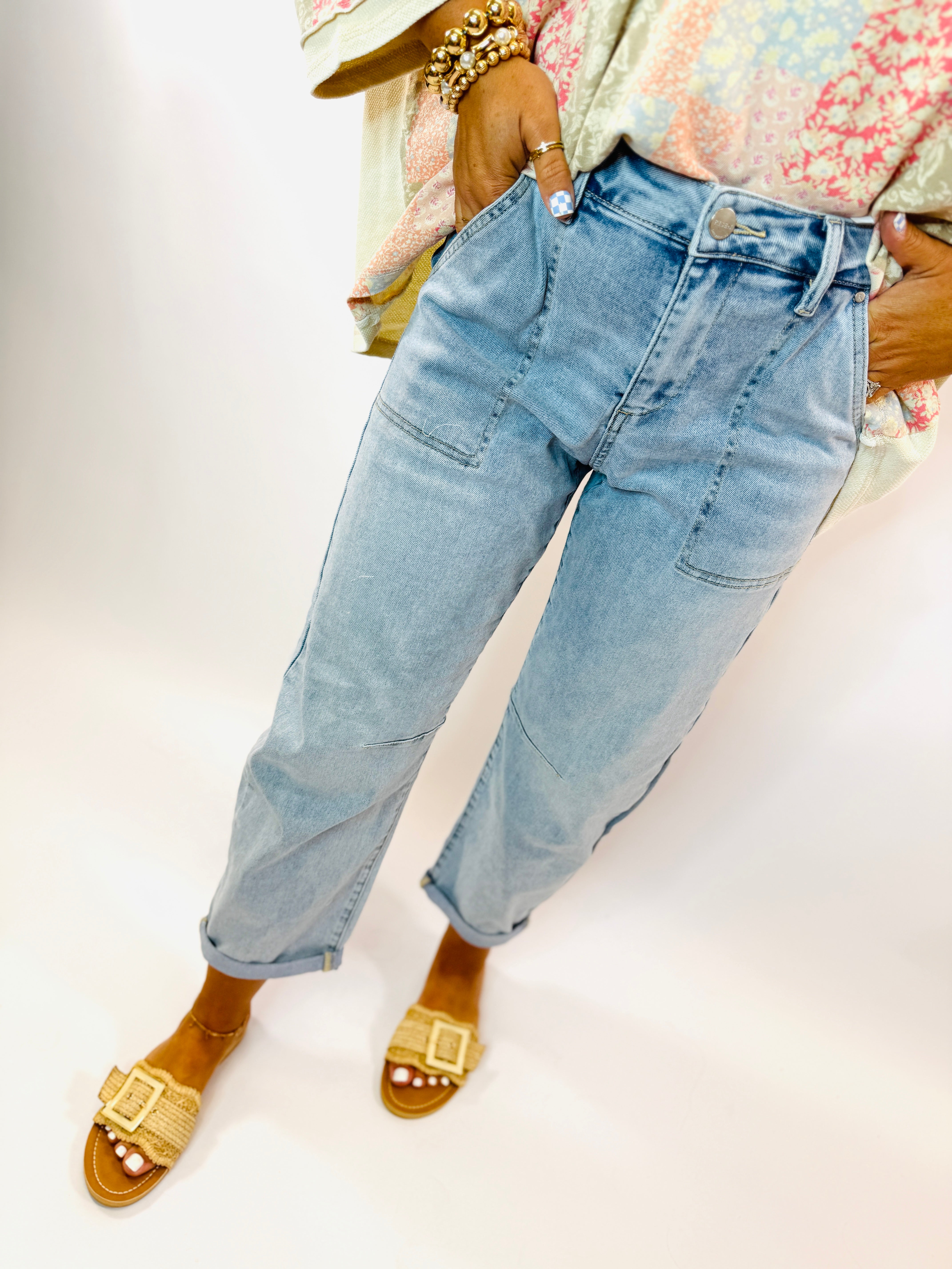 Woman wearing light blue relaxed-fit Soleil jeans with rolled cuffs, paired with gold woven sandals and beaded bracelets.