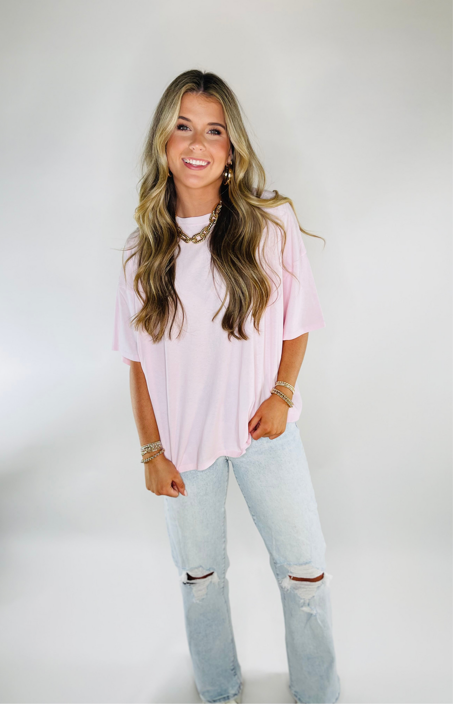 Woman wearing pink oversized Danna top with light wash distressed jeans and gold jewelry accessories.