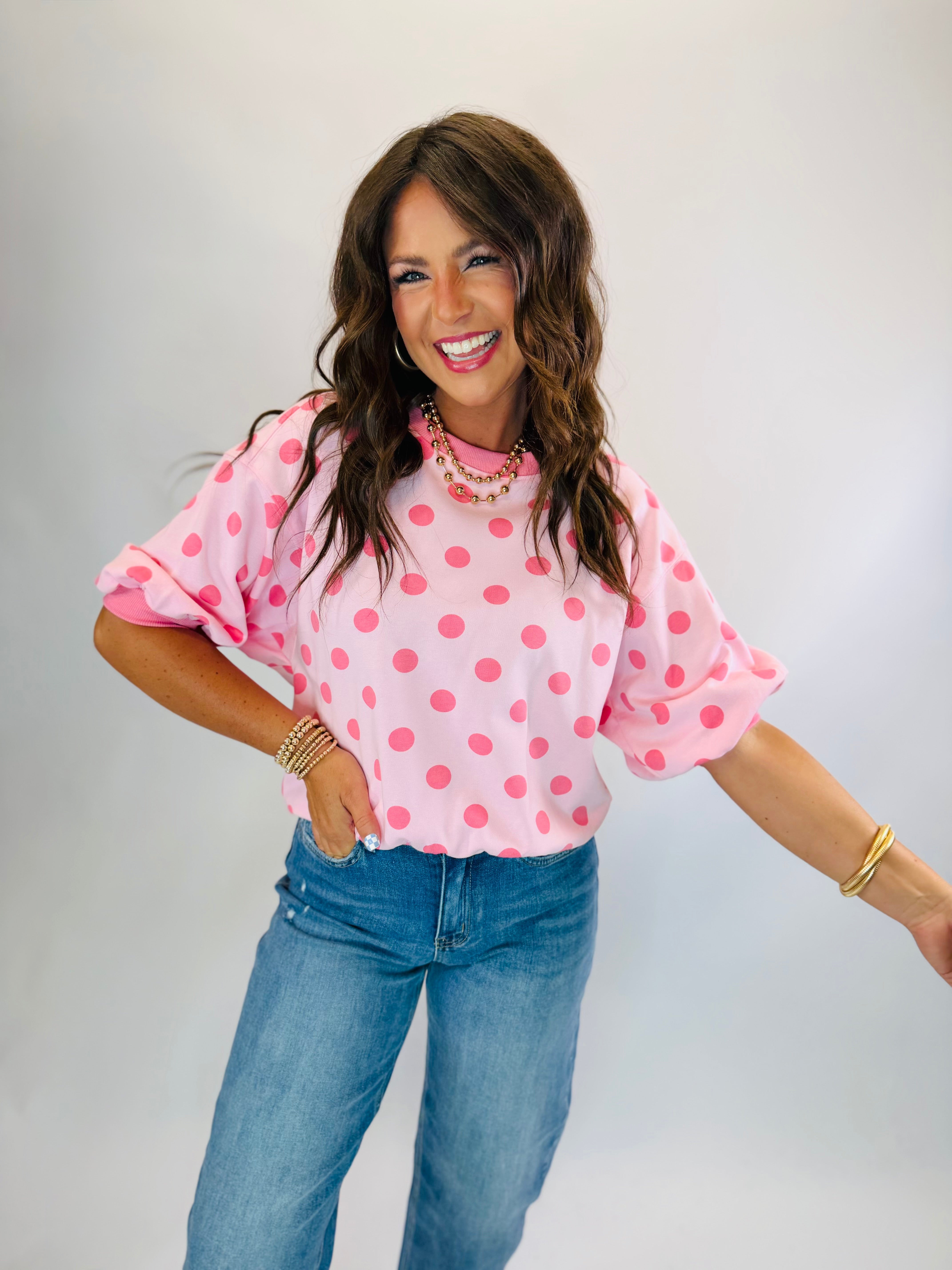 Woman wearing Parker Top in light pink with hot pink polka dots, paired with blue jeans.