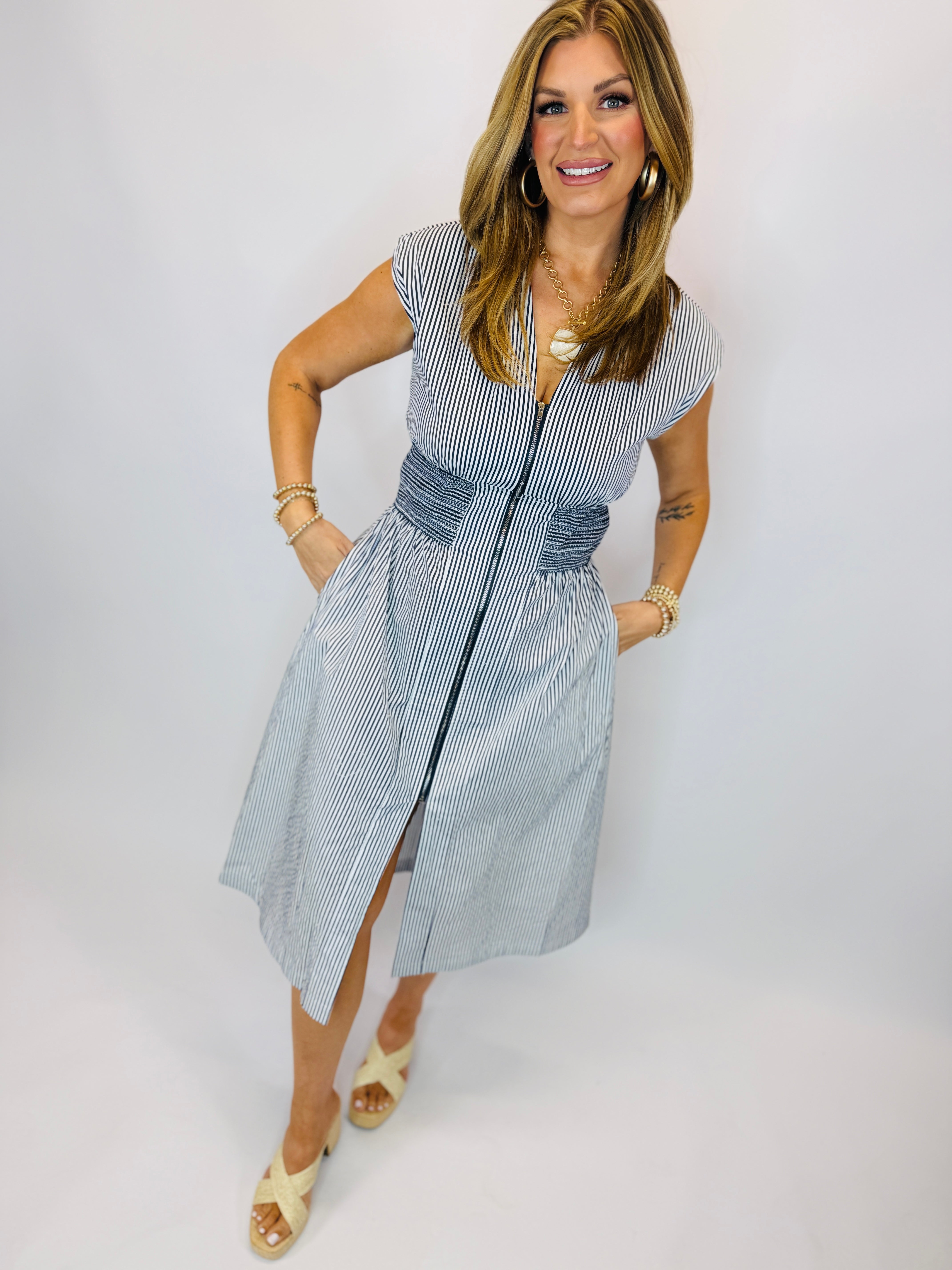 Woman wearing blue and white striped button-front midi dress with short sleeves and tie waist detail.