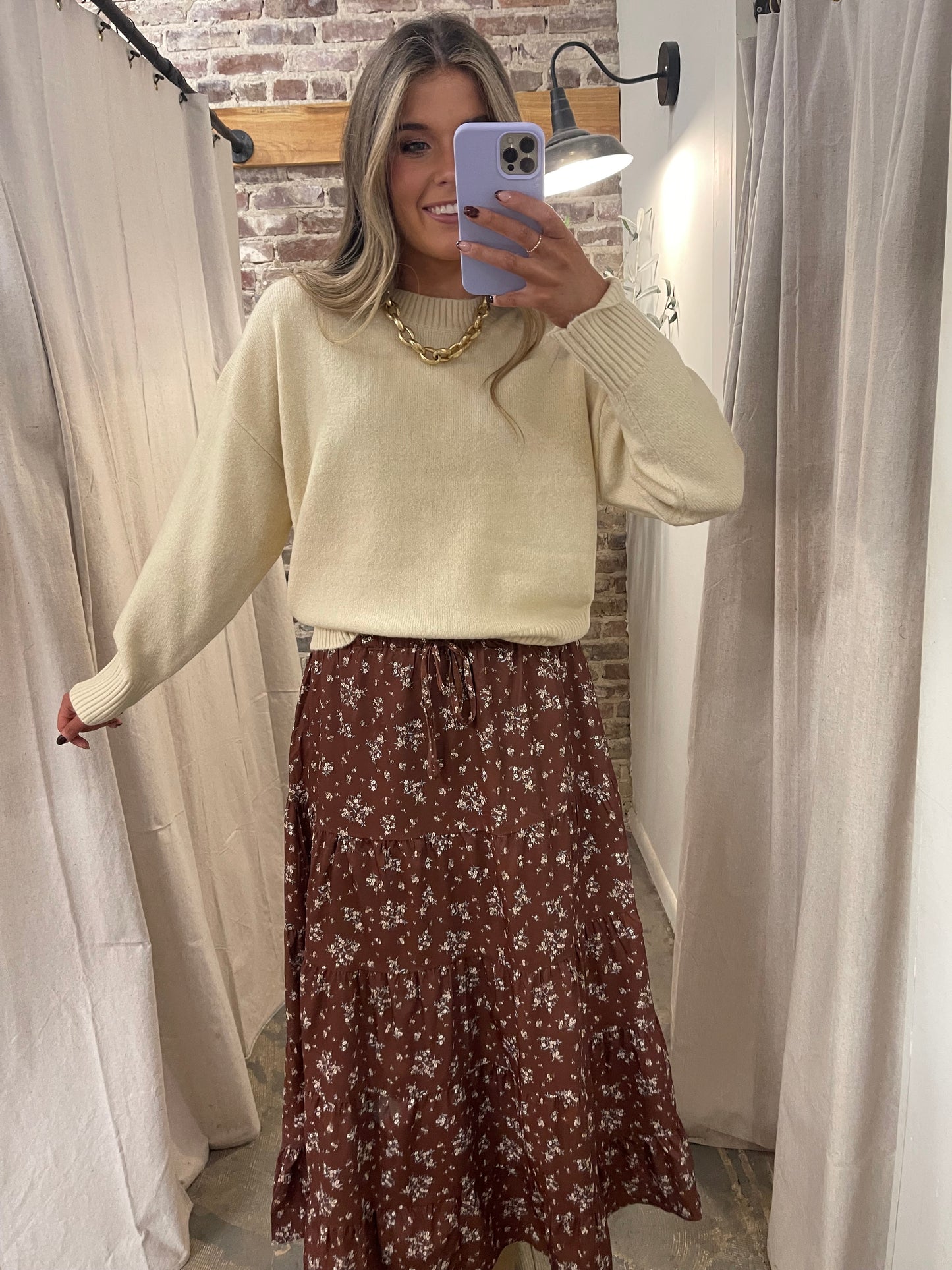 Woman wearing cream knit Emory sweater with gold chain necklace and brown floral midi skirt