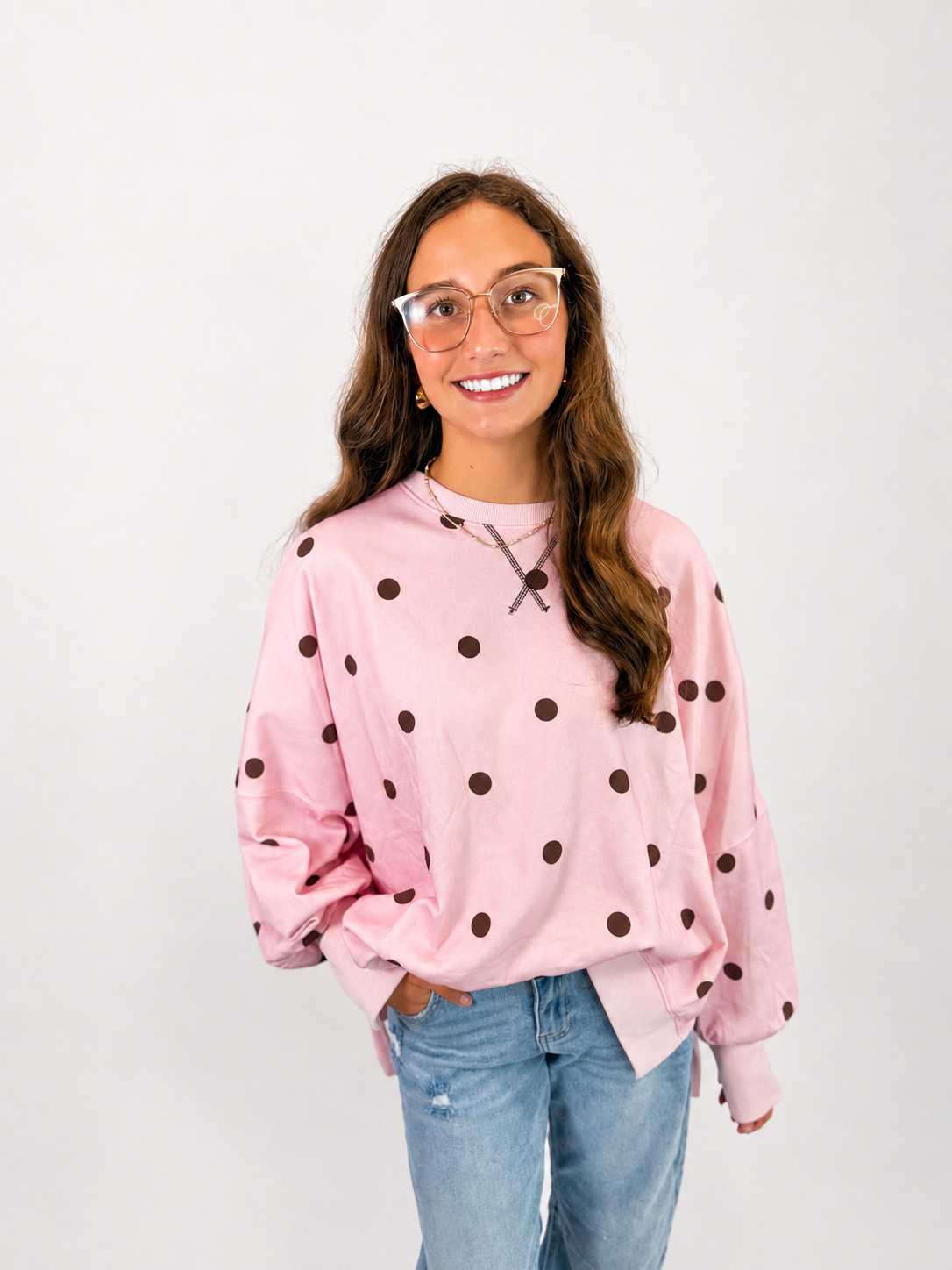 Pink polka dot oversized sweatshirt with brown dots, paired with light wash jeans and glasses.
