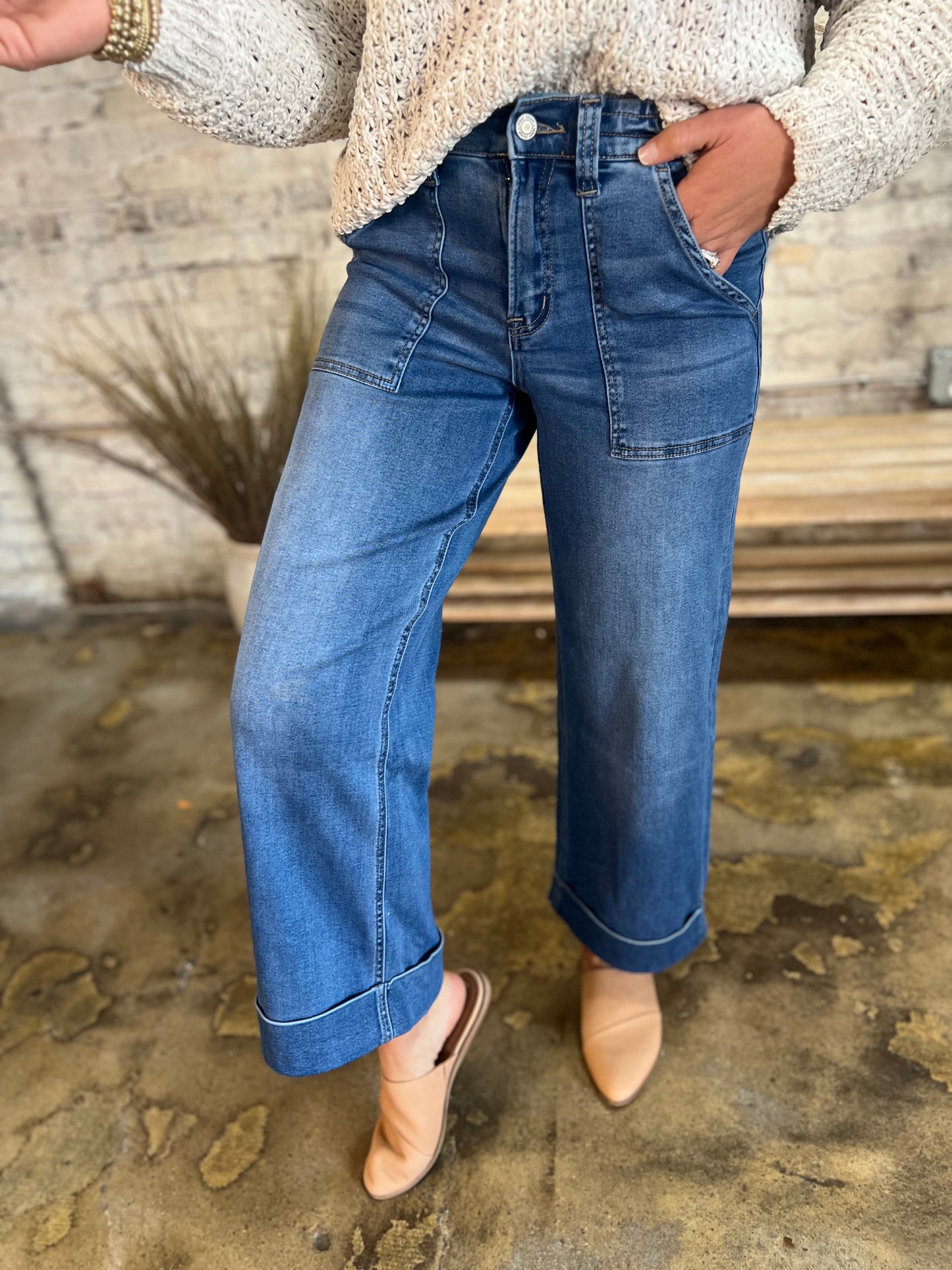 Woman wearing wide-leg cropped denim jeans with cuffed hems and front pockets, paired with tan shoes.