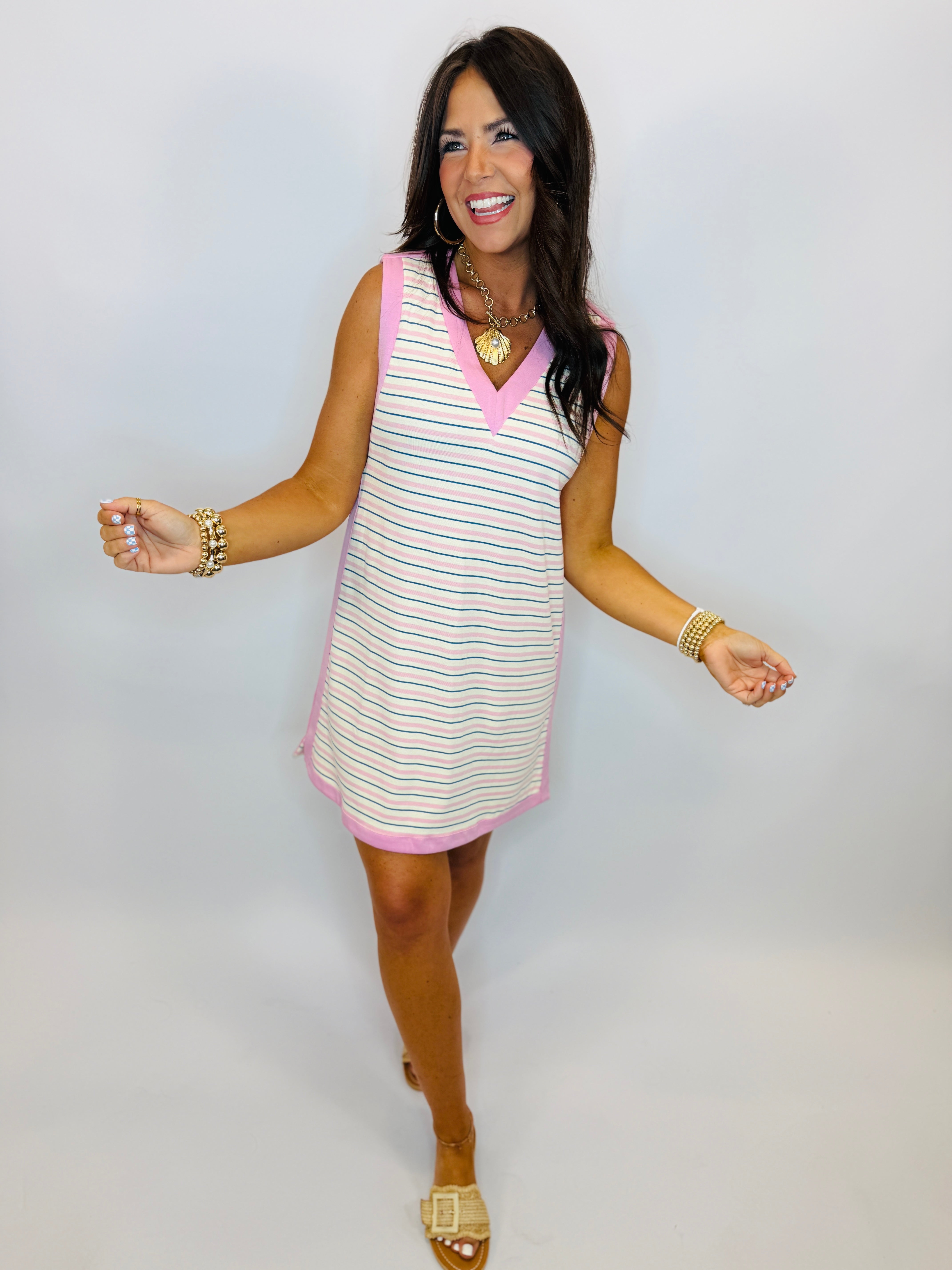 Woman wearing pink and teal striped sleeveless v-neck dress with gold jewelry and sandals