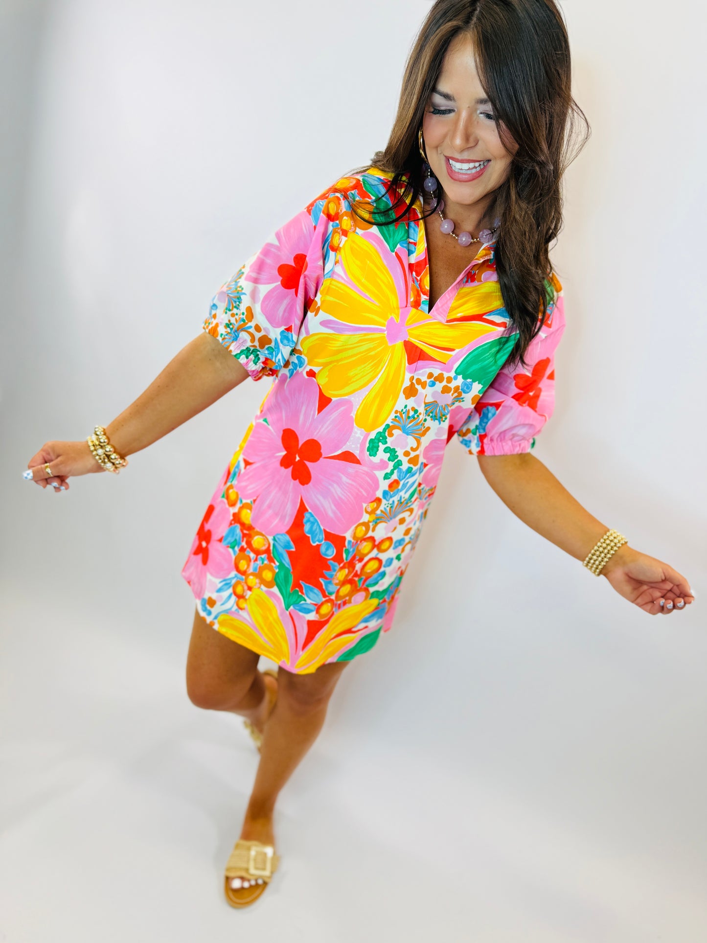 Woman wearing vibrant tropical floral print dress with short sleeves and collar, styled with gold jewelry and sandals.