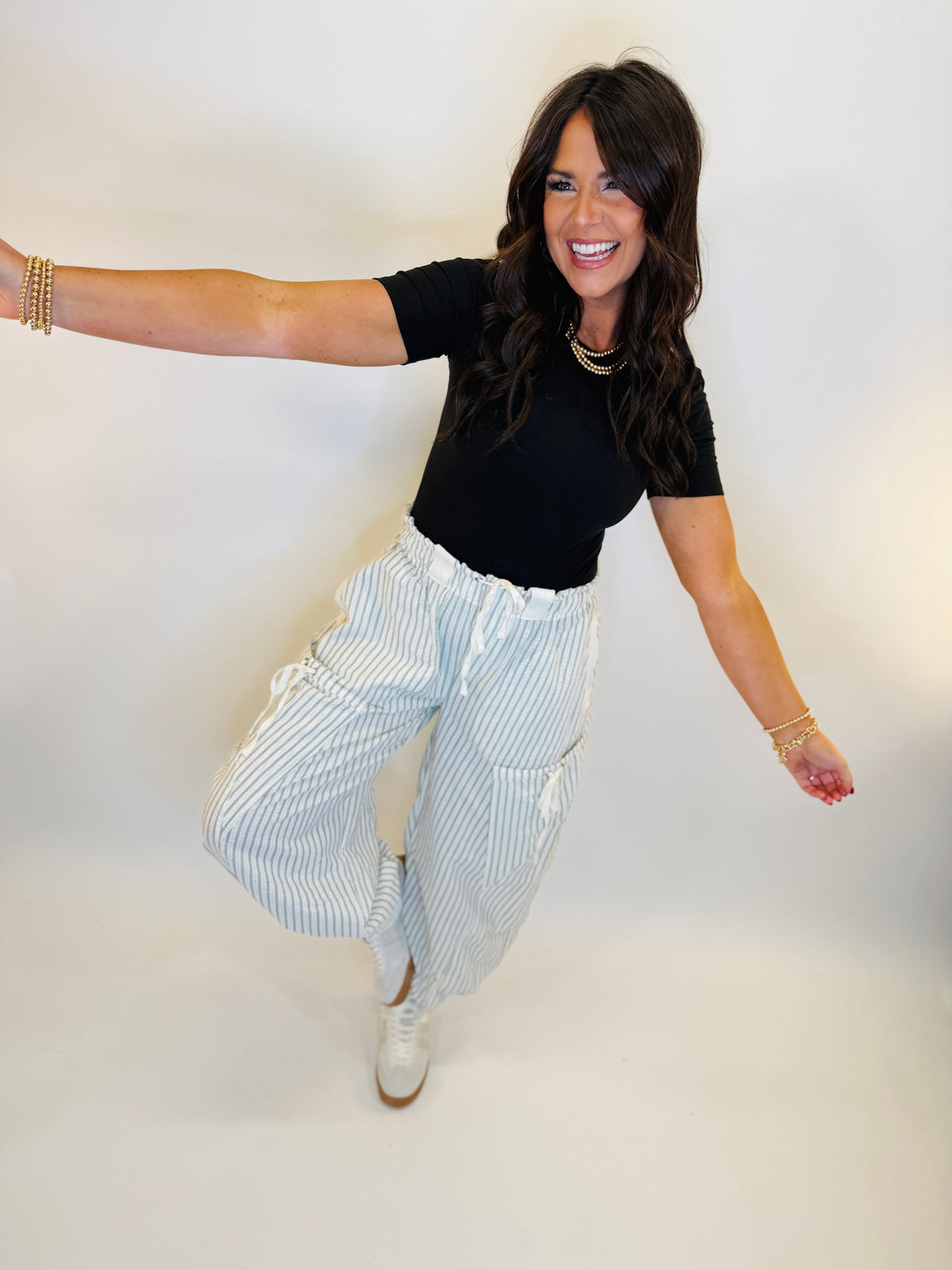 Woman wearing black short-sleeve Jenny top with pearl necklace, styled with striped pants and gold bracelets