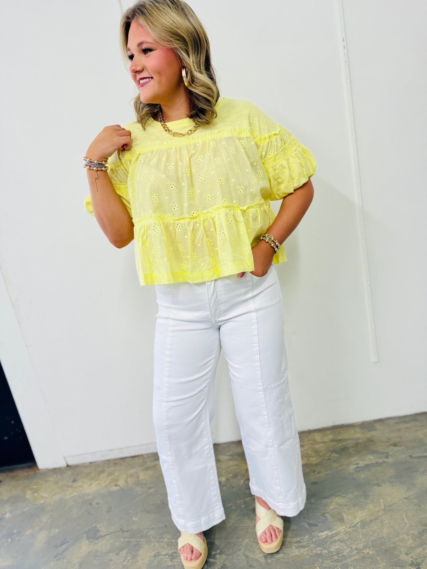 Woman wearing yellow eyelet top with white wide-leg structured pants and platform sandals