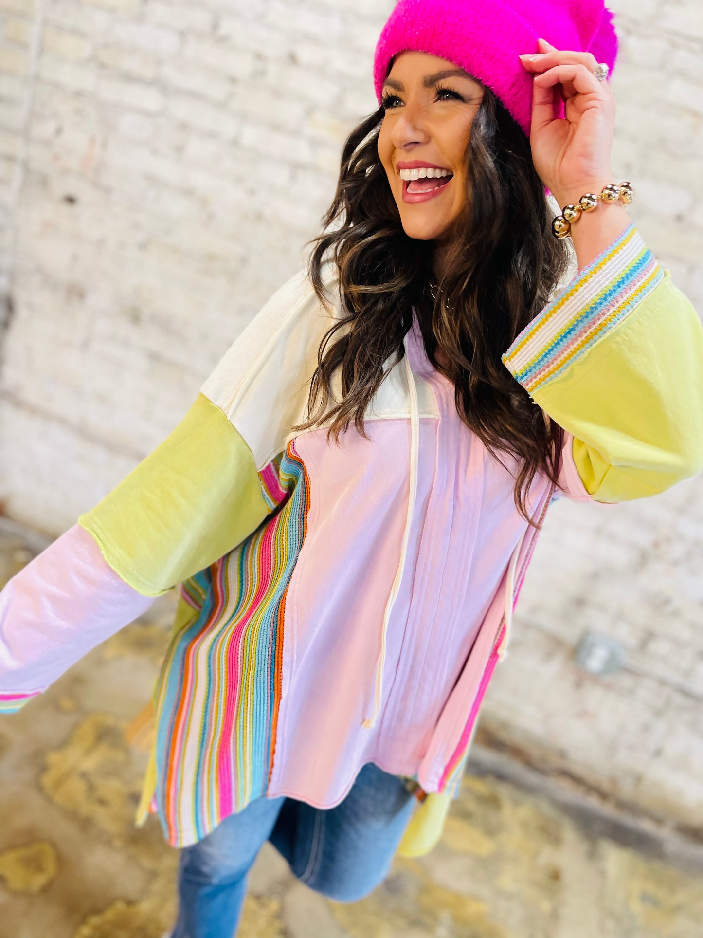 Woman wearing colorful striped long sleeve Ember hoodie with pink beanie, smiling outdoors