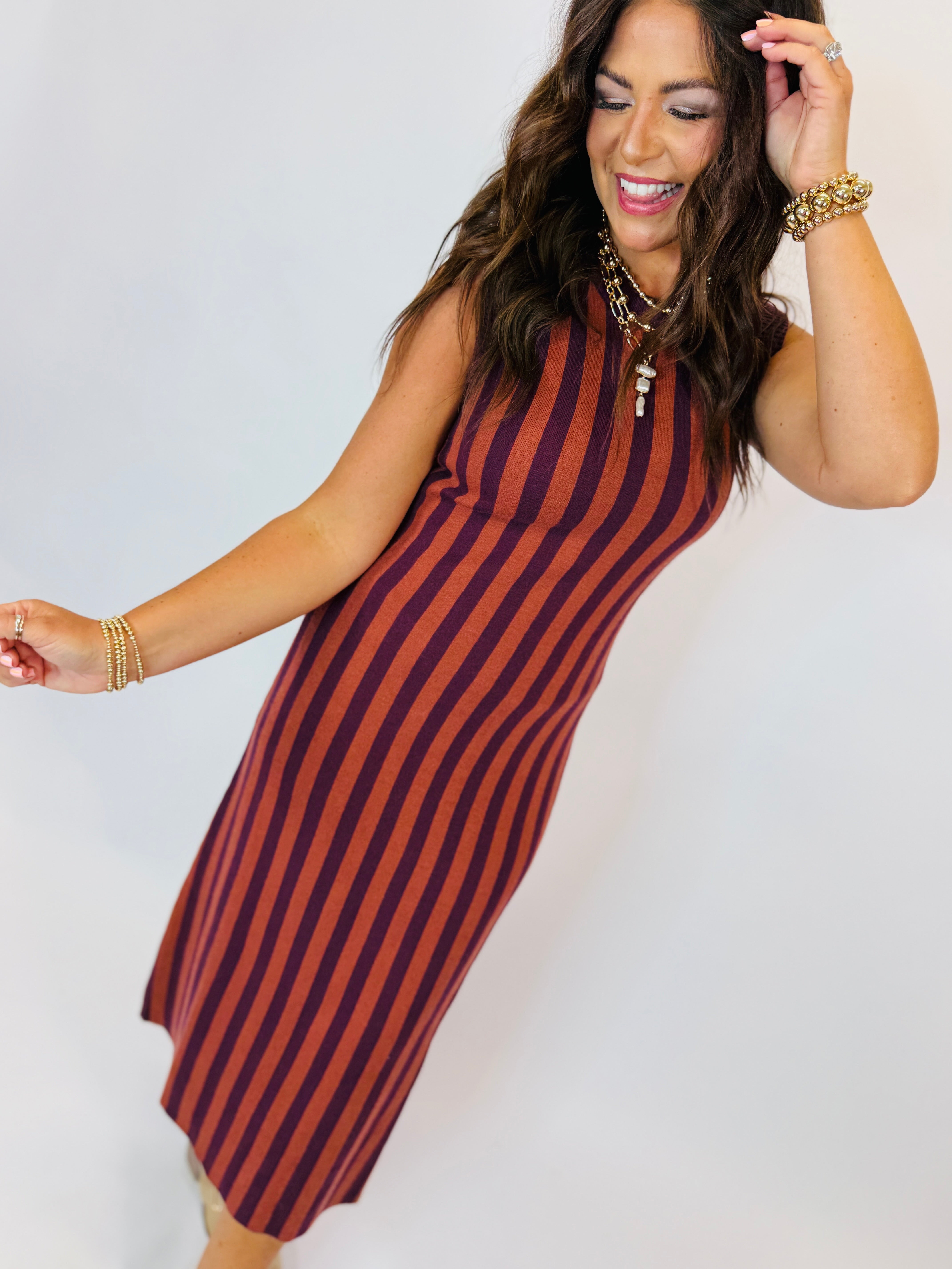 Woman wearing Darcy sleeveless striped midi dress in rust orange and burgundy with gold accessories.