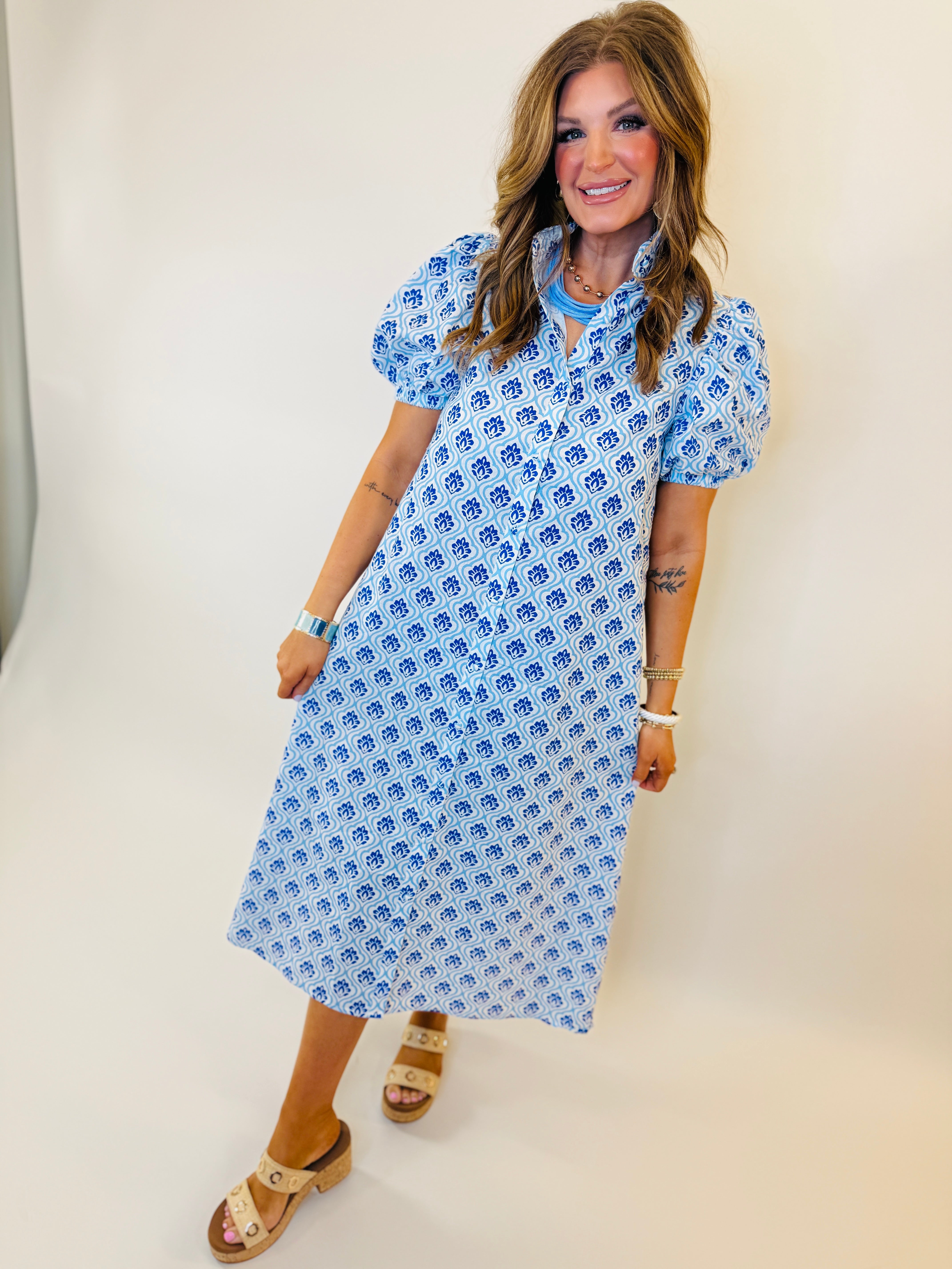 Woman wearing blue and white patterned midi dress with short sleeves and tie neck detail.