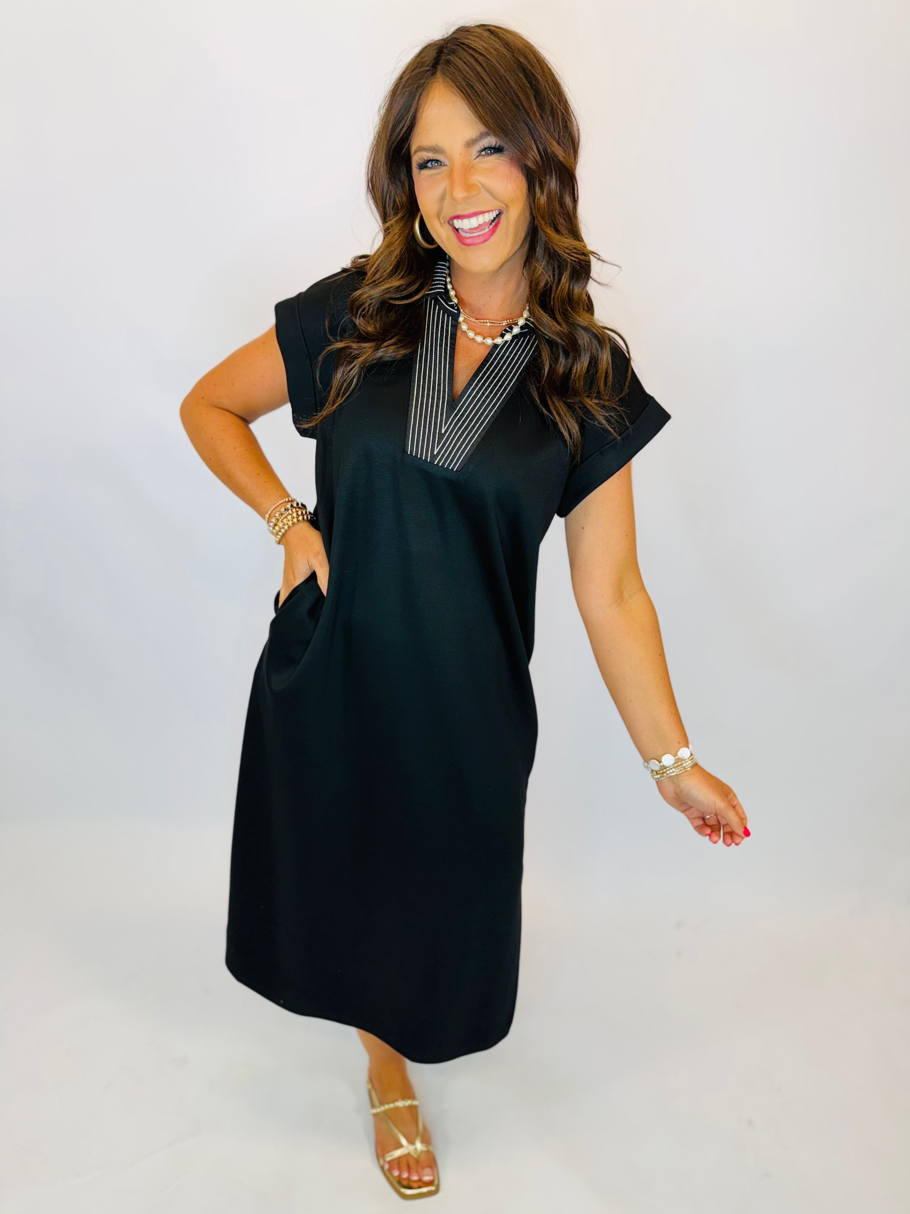 Black midi shift dress with striped V-neckline collar, short sleeves, and side pockets, styled with gold sandals.