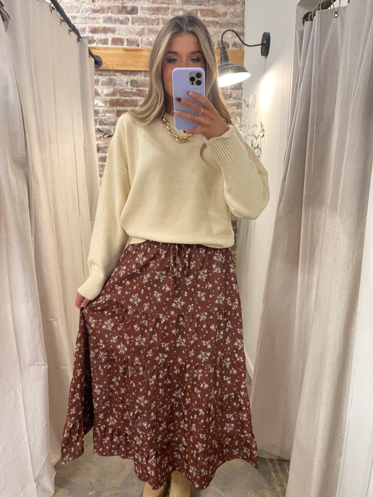 Woman wearing cream oversized knit sweater with floral midi skirt, taking mirror selfie in fitting room