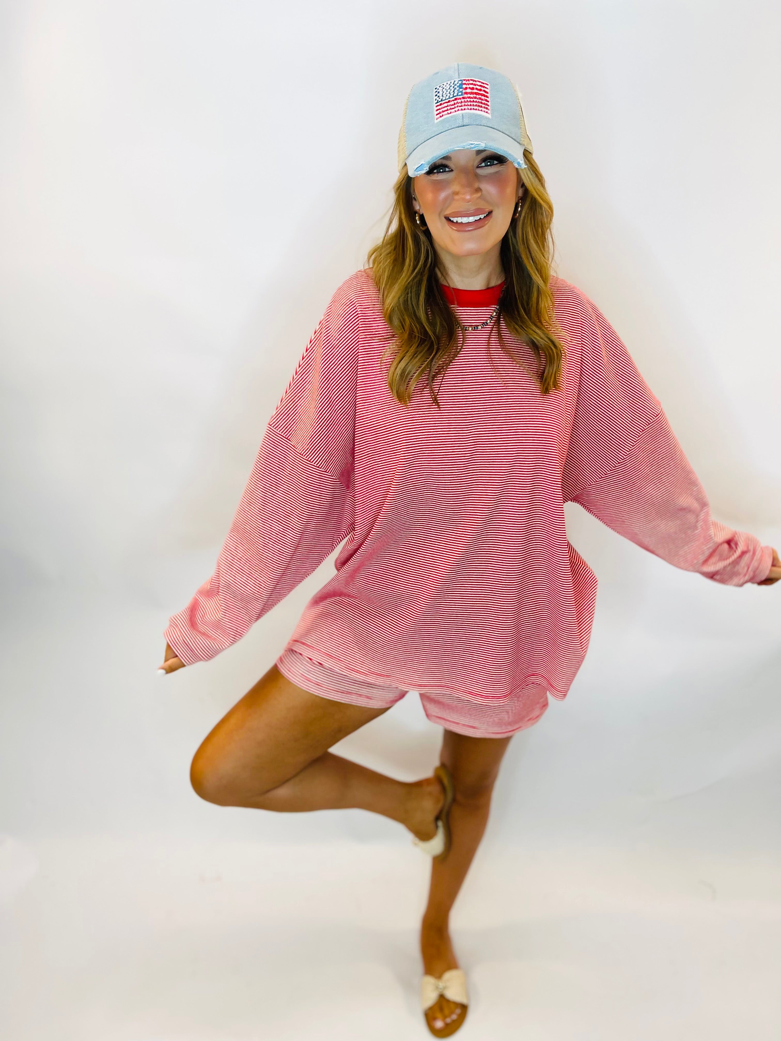 Woman wearing oversized red and white striped long-sleeve top with matching shorts and American flag cap.
