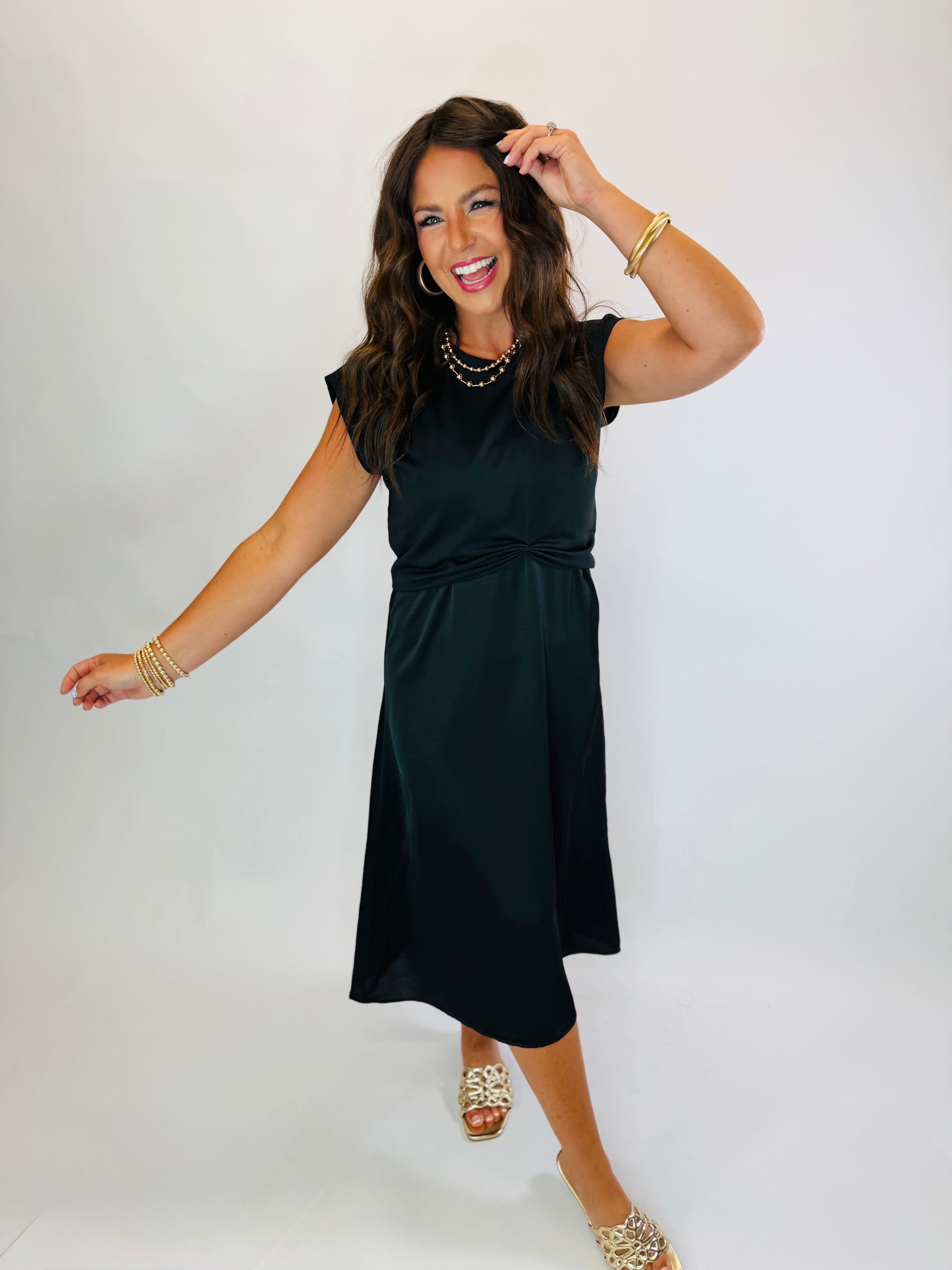 Woman wearing a black midi-length satin Gracie Dress with cap sleeves and cinched waist detail.