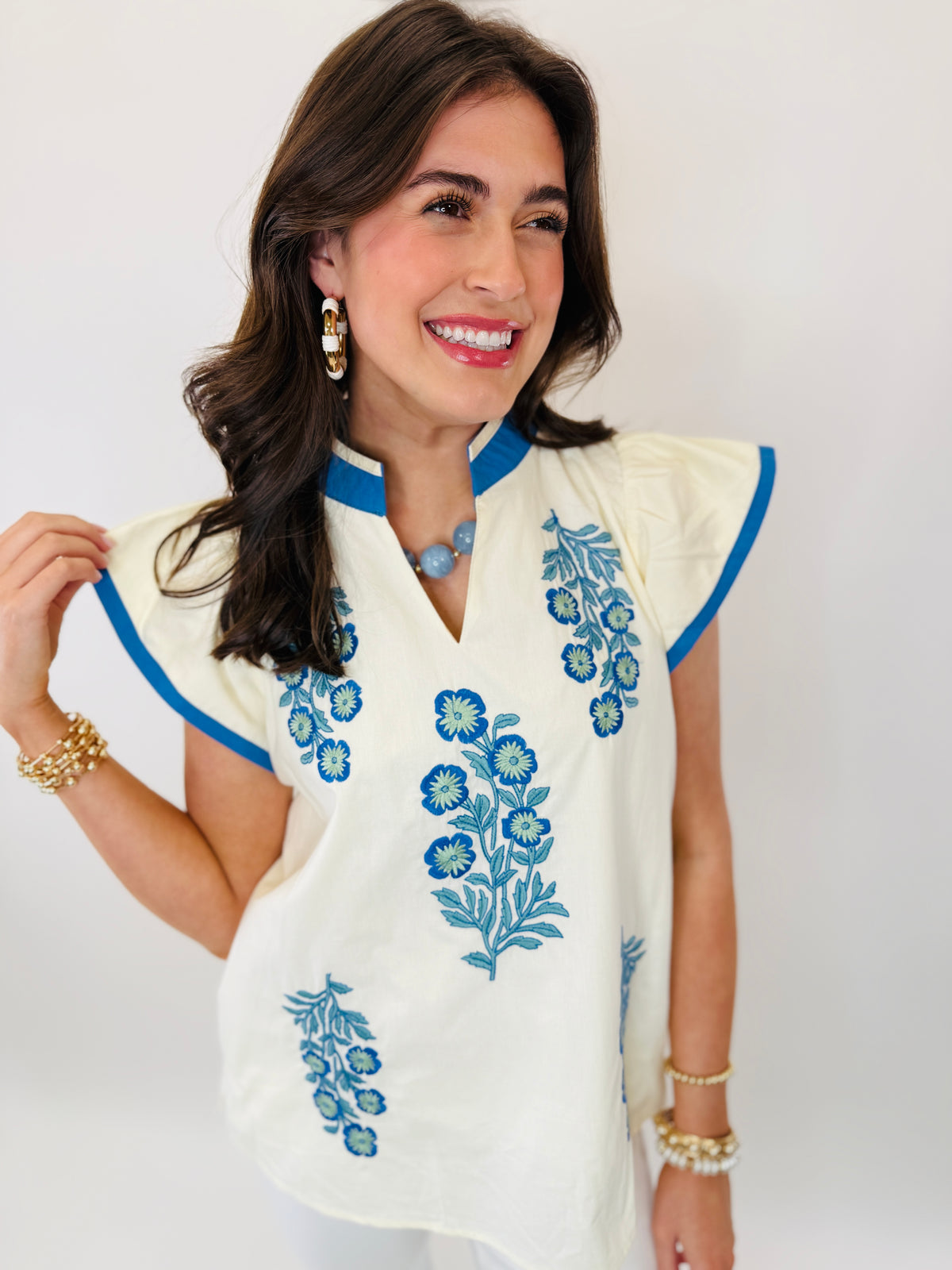 Woman wearing white embroidered top with blue floral patterns, short sleeves, and blue trim details.