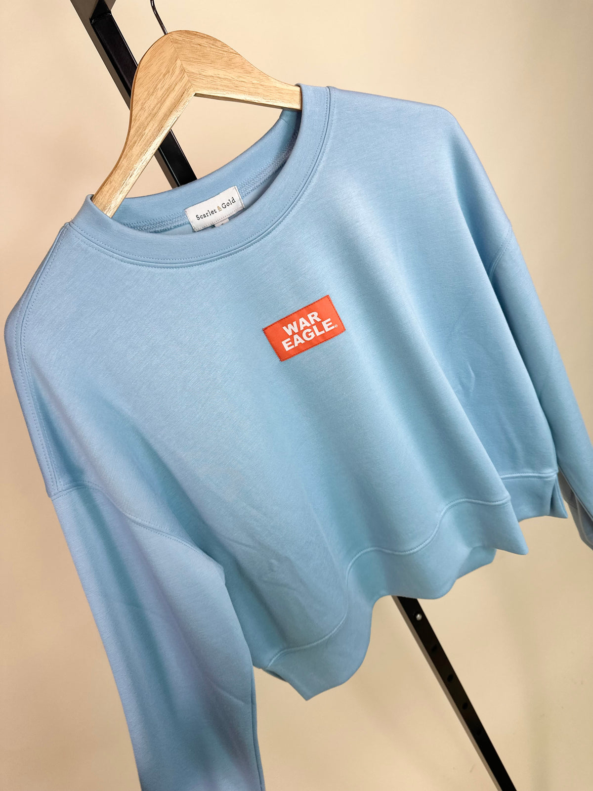 Light blue cropped crewneck sweatshirt with orange "War Eagle" woven label patch on chest.