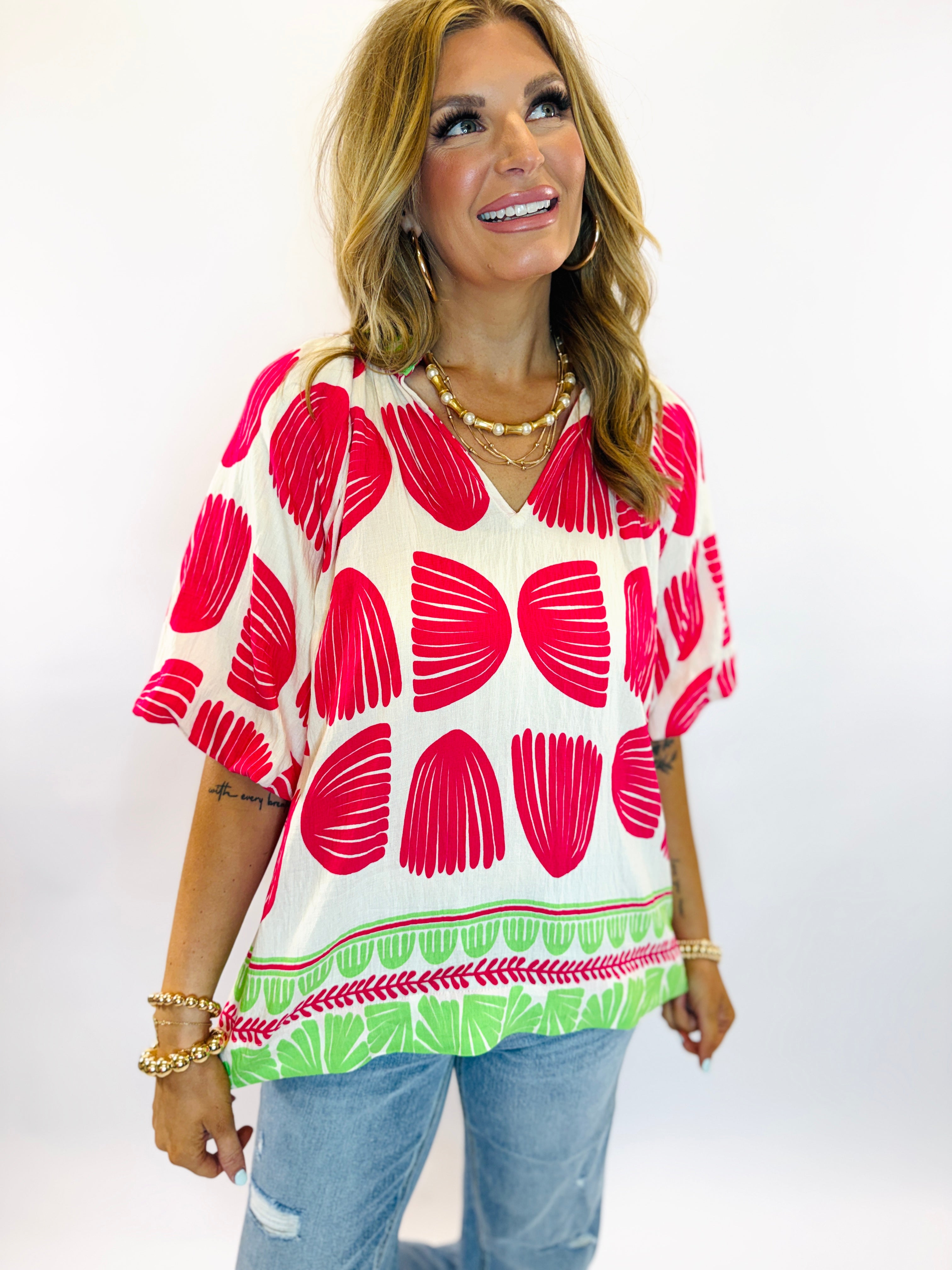 Woman wearing vibrant Rosa top with red floral pattern, green leaf border trim, and short sleeves