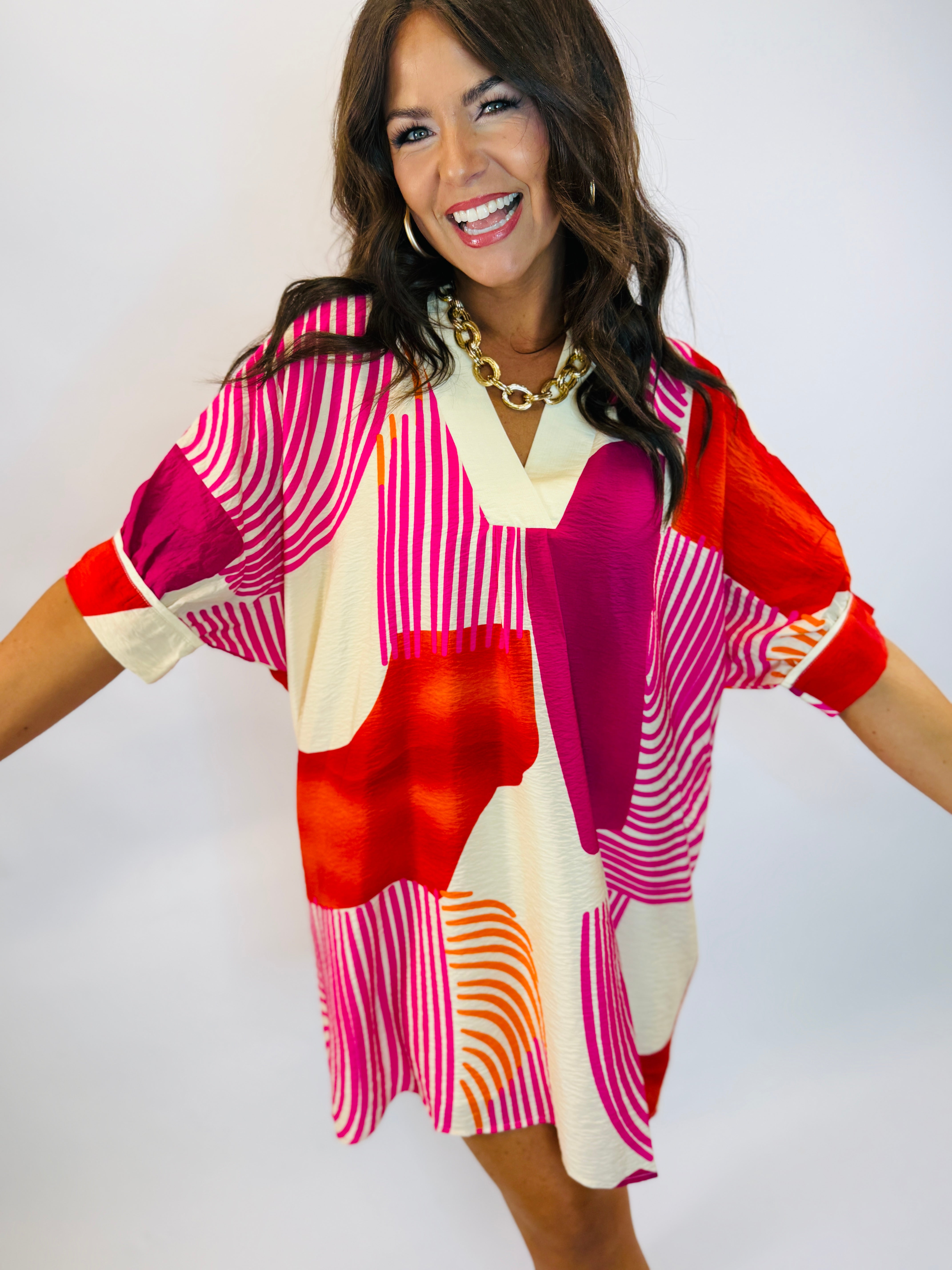 Woman wearing colorful geometric print dress with pink, red, orange and cream patterns in relaxed fit style.