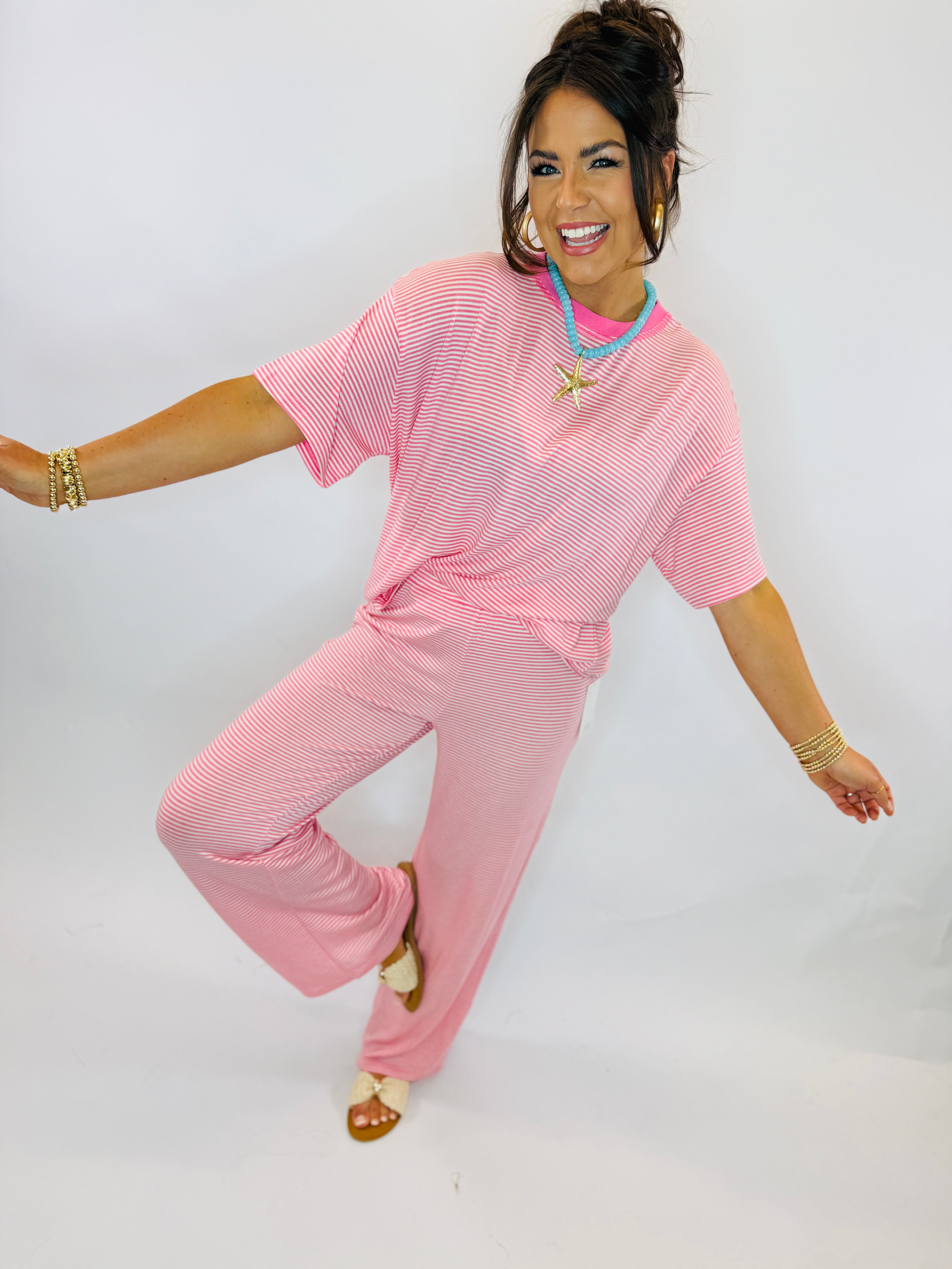 Woman wearing pink striped ribbed two-piece set with matching top and wide-leg pants, styled with turquoise necklace and g...