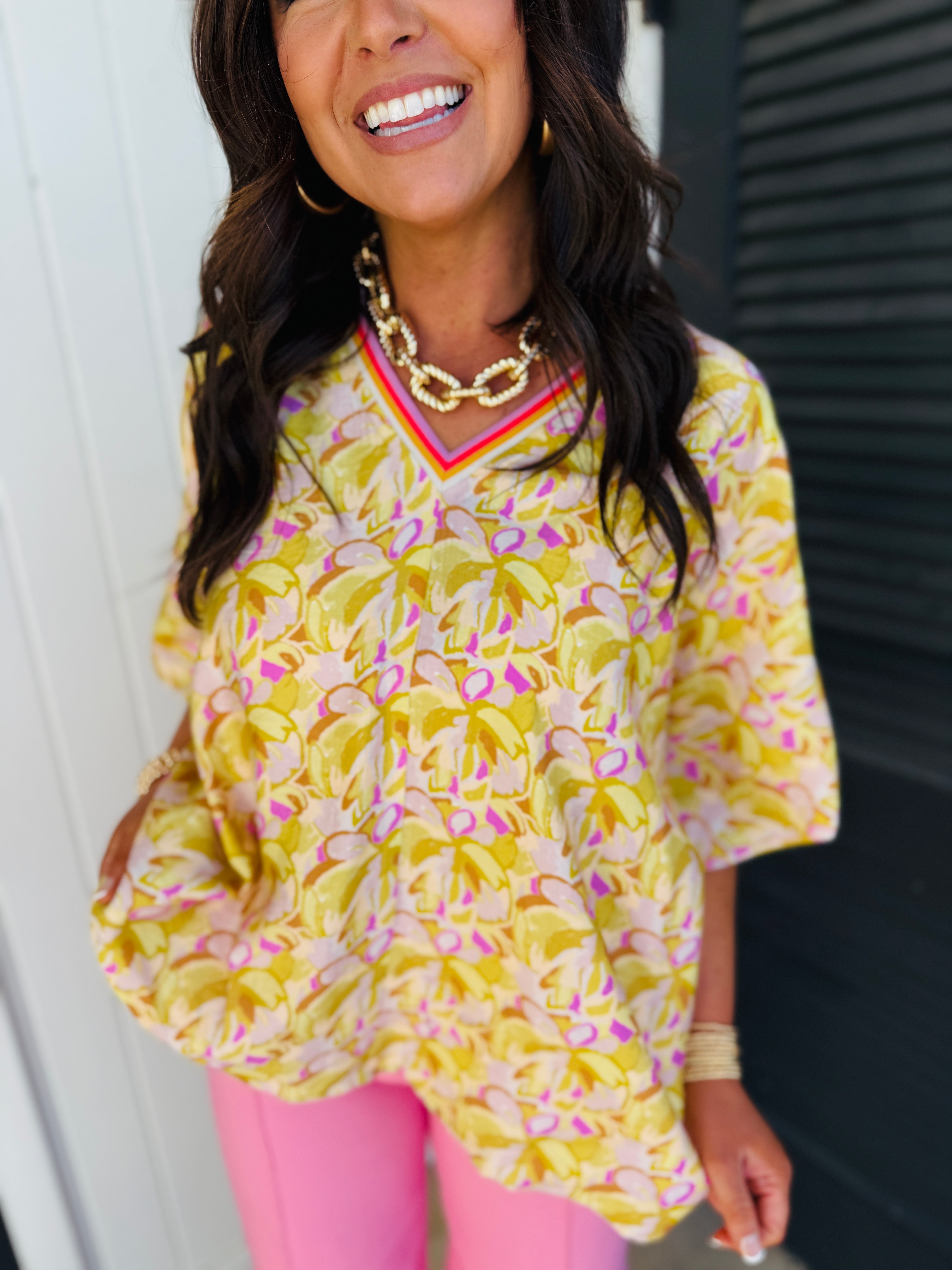 Woman wearing yellow floral print Arabella Harper soft top with pink trim and gold chain necklace.