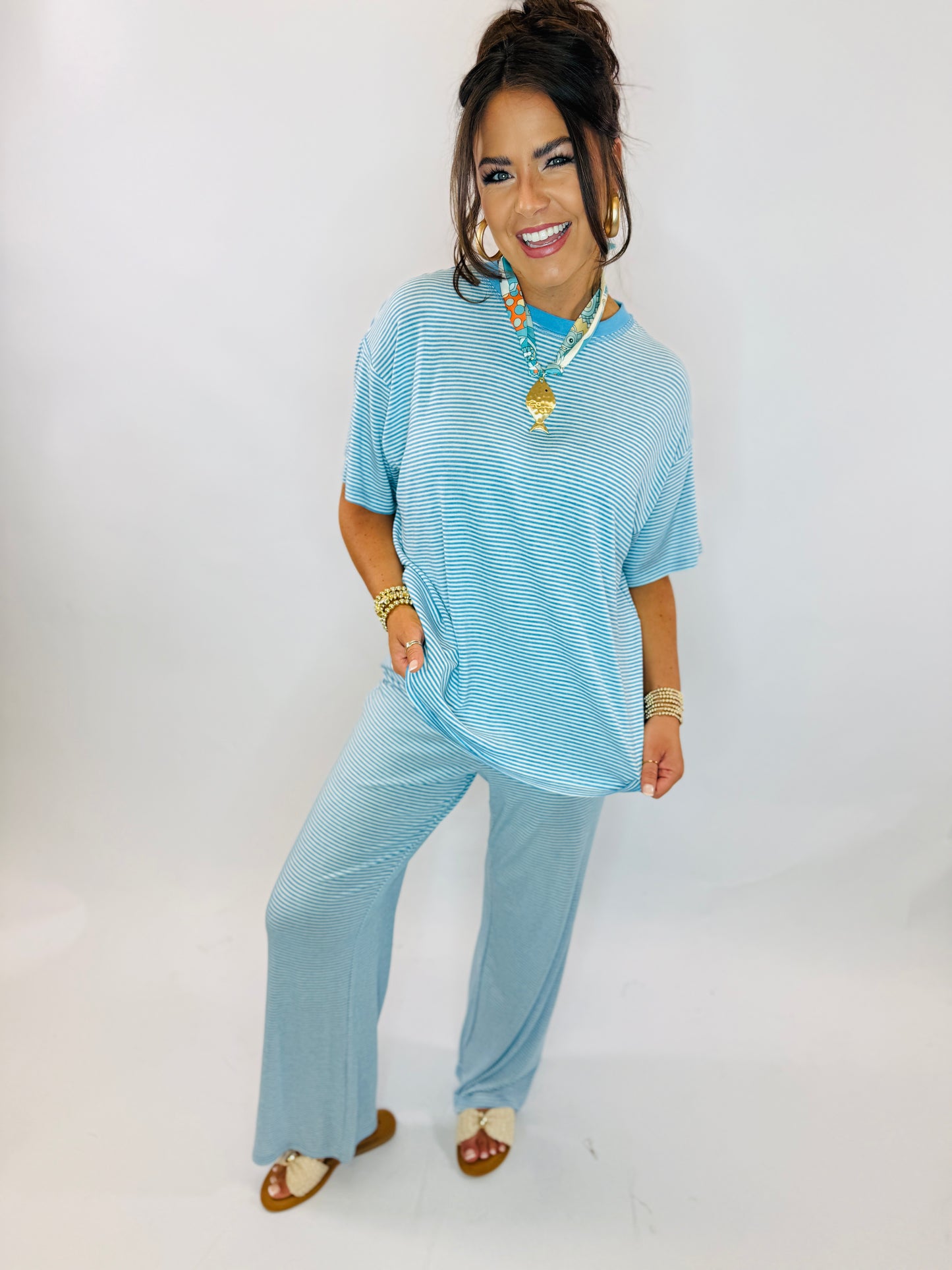 Woman wearing blue striped matching set with short-sleeve top and wide-leg pants, accessorized with jewelry and sandals.