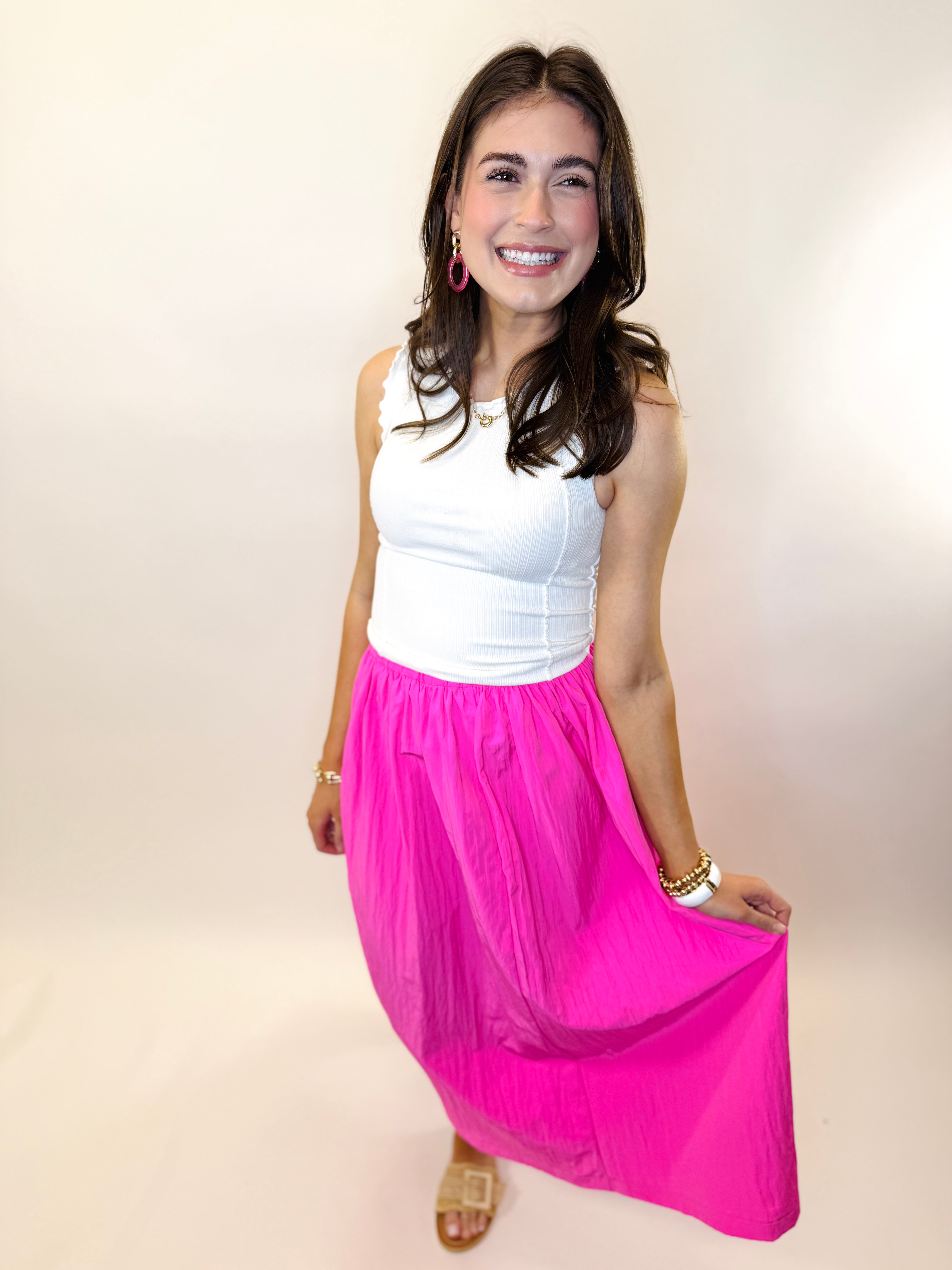 Woman wearing bright pink maxi skirt with white tank top, smiling and posing against neutral background.