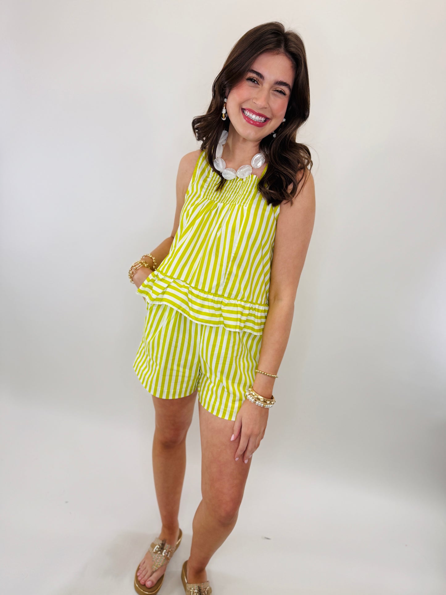 Woman wearing yellow and white striped sleeveless top with matching shorts, gold accessories and sandals.