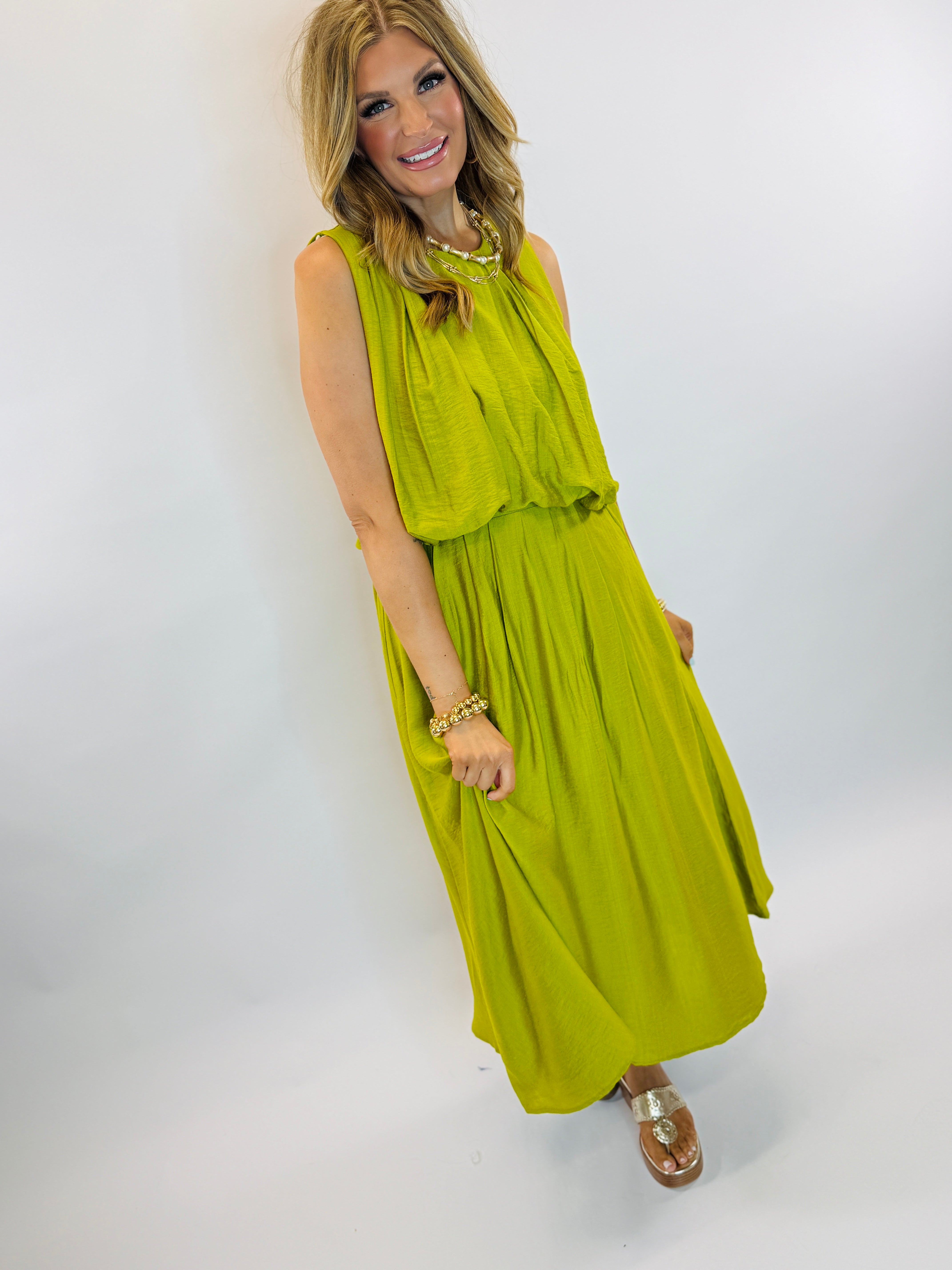 Woman wearing lime green sleeveless maxi dress with gathered waist, paired with gold jewelry and sandals.