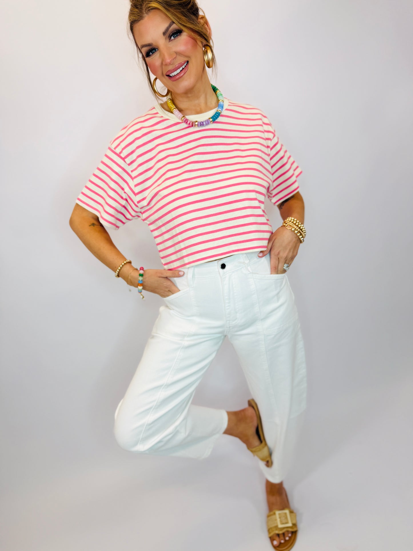 Woman wearing pink and white striped oversized t-shirt with white jeans and colorful beaded necklace