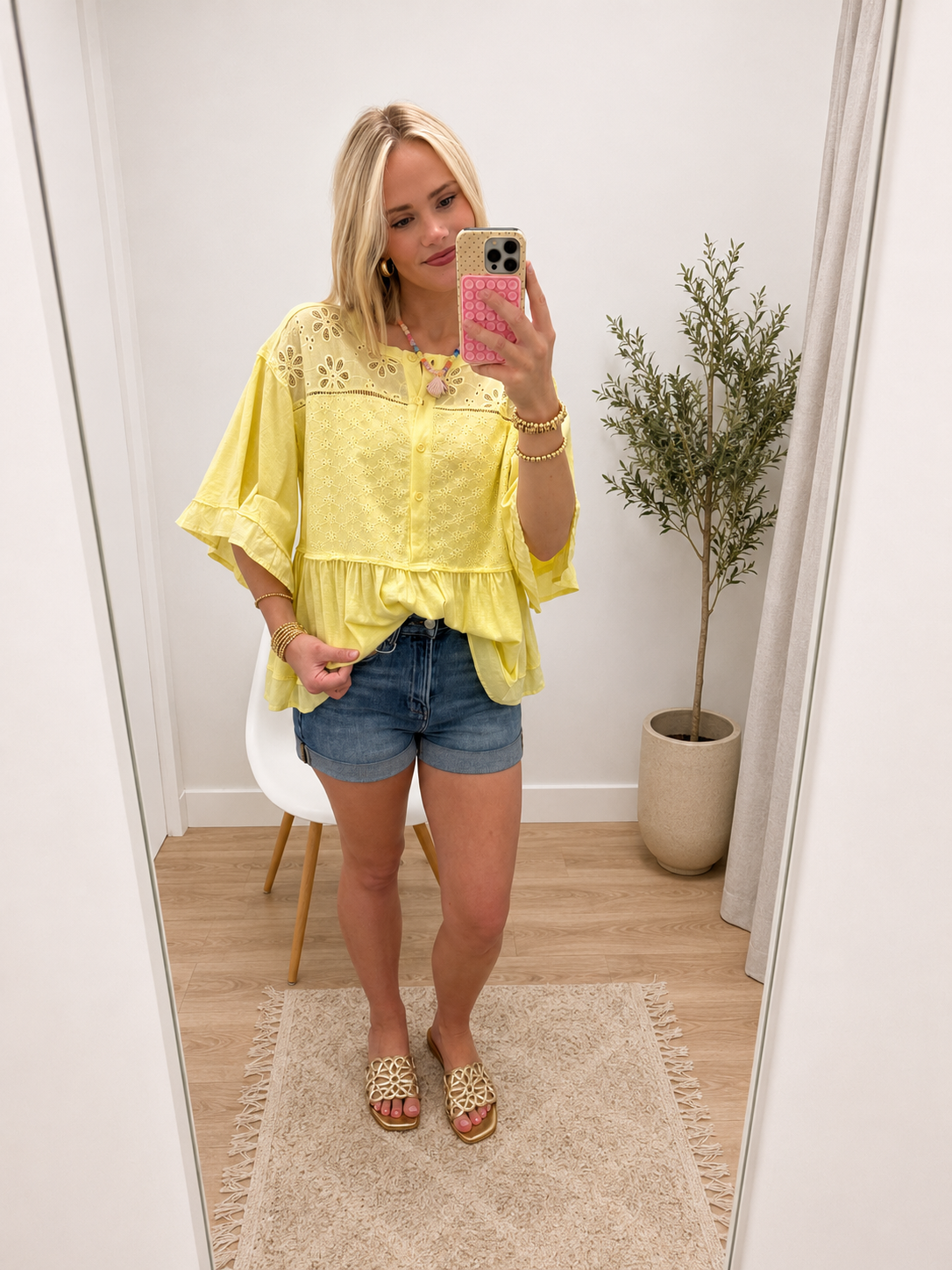 Yellow eyelet lace peplum top with flutter sleeves and button-front detail, styled with denim shorts.