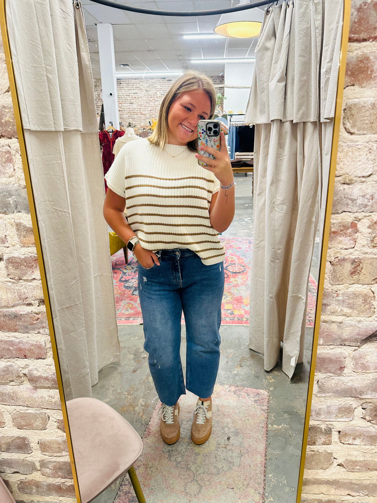 Woman wearing striped sweater and blue Lexi denim jeans taking mirror selfie in fitting room