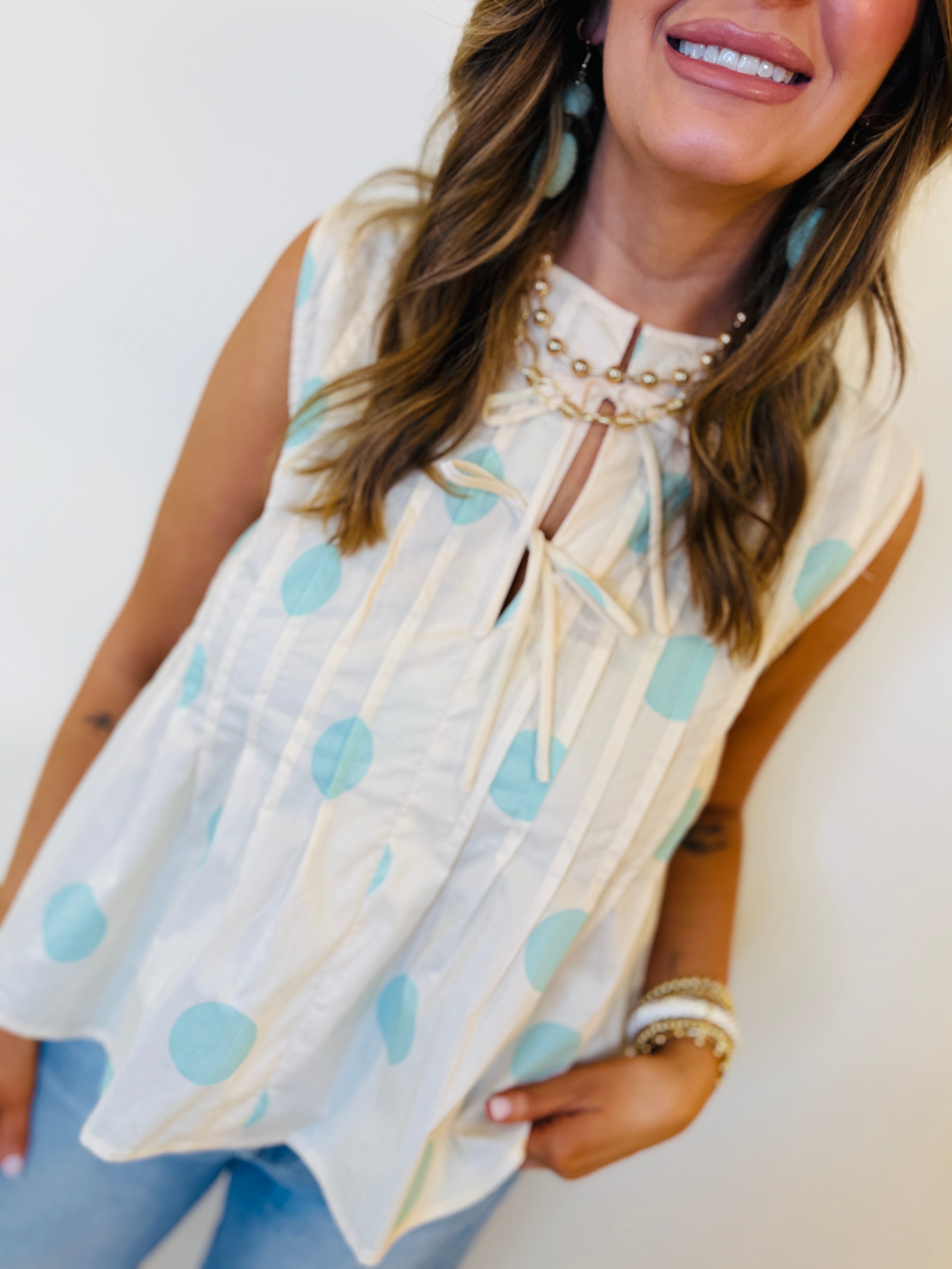 Woman wearing white sleeveless polka dot top with blue dots, pearl collar detail, and keyhole neckline