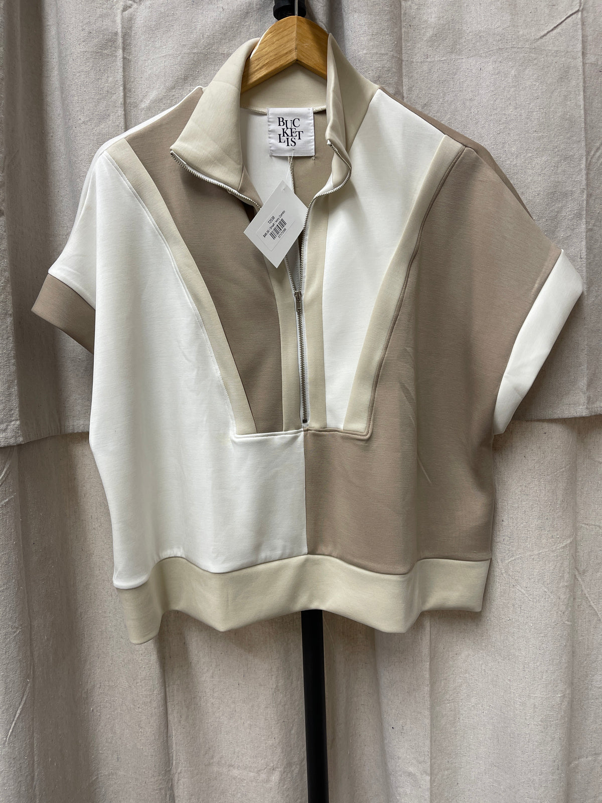 Cream colored Linda Top with half-zip collar and short sleeves hanging on wooden hanger with price tag.