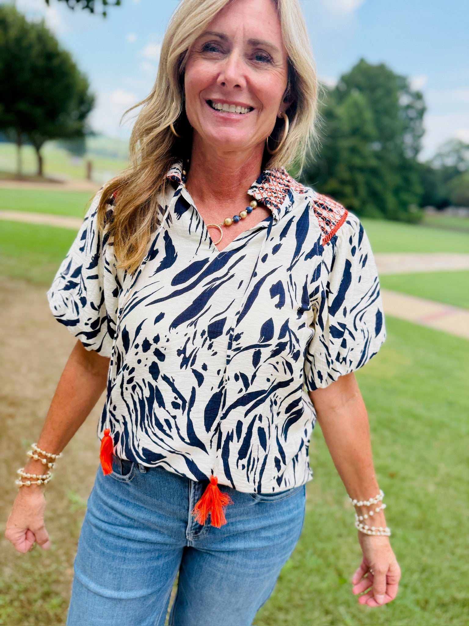 Woman wearing Rita Top, white and navy abstract print blouse with orange tassels and embroidered shoulders.