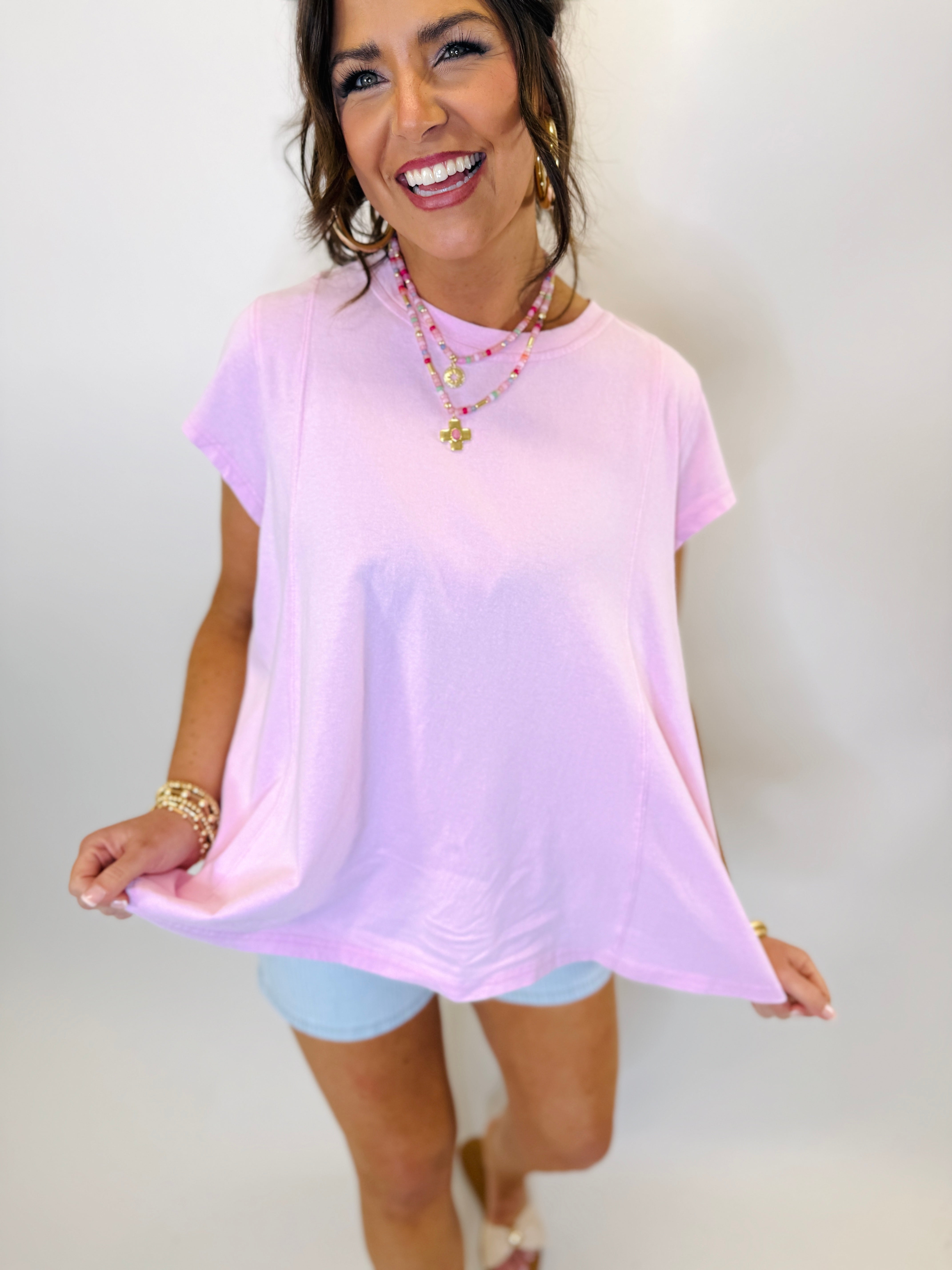 Woman wearing pink tie-dye oversized short sleeve top with layered necklaces and denim shorts