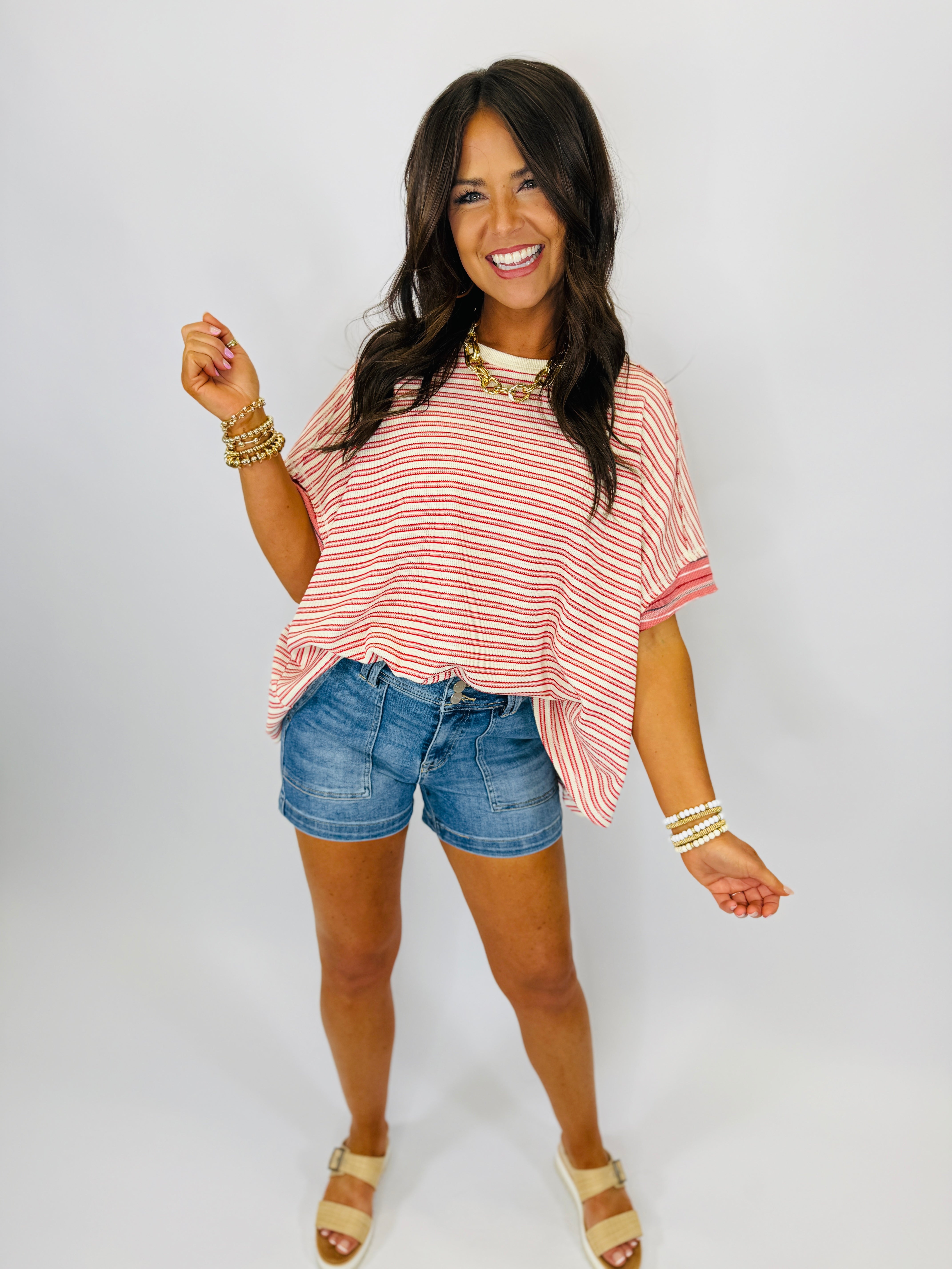 Woman wearing pink and white striped oversized top with denim shorts and gold jewelry accessories