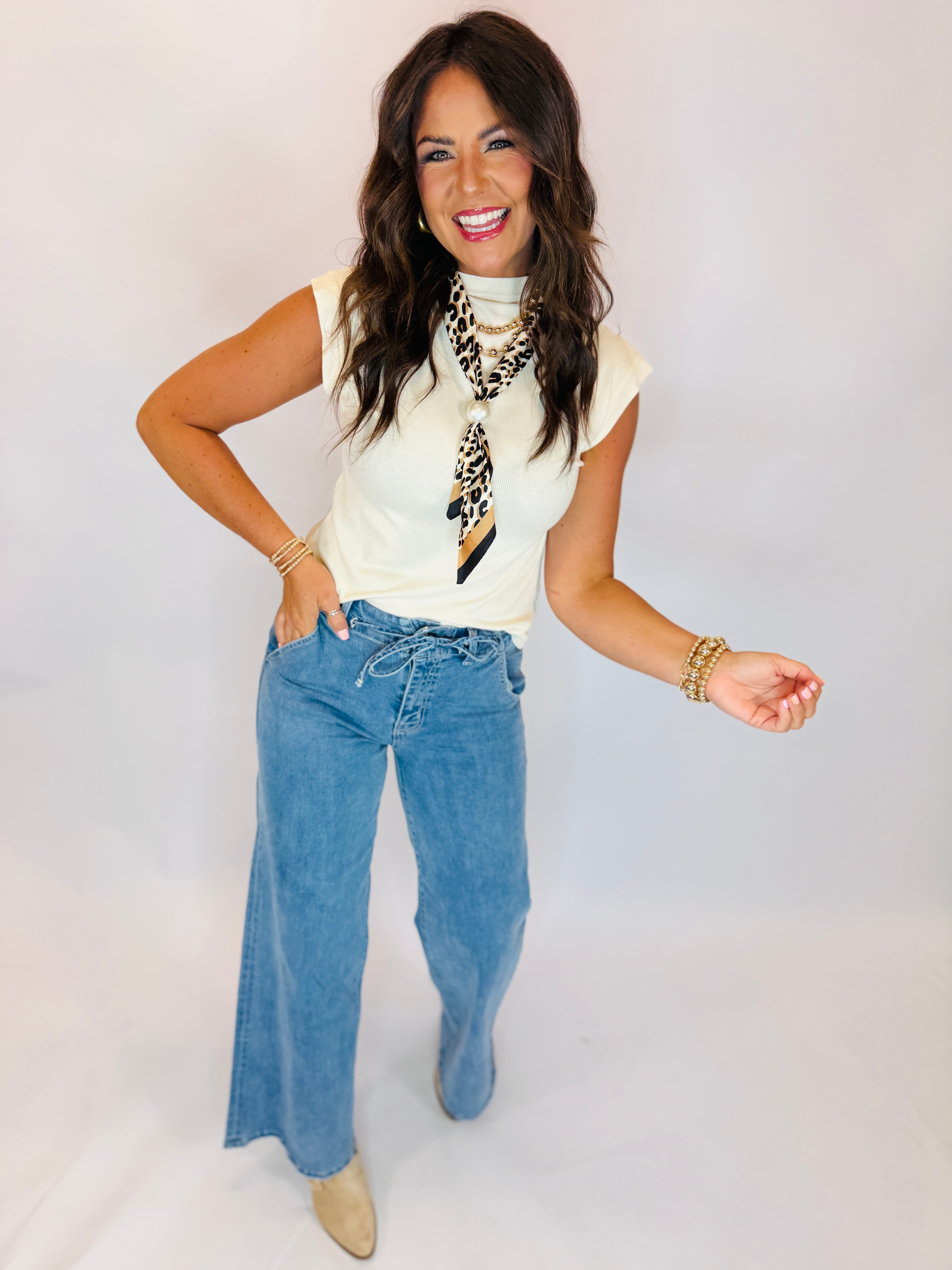Ivory sleeveless mock-neck ribbed top styled with wide-leg jeans and leopard print scarf.
