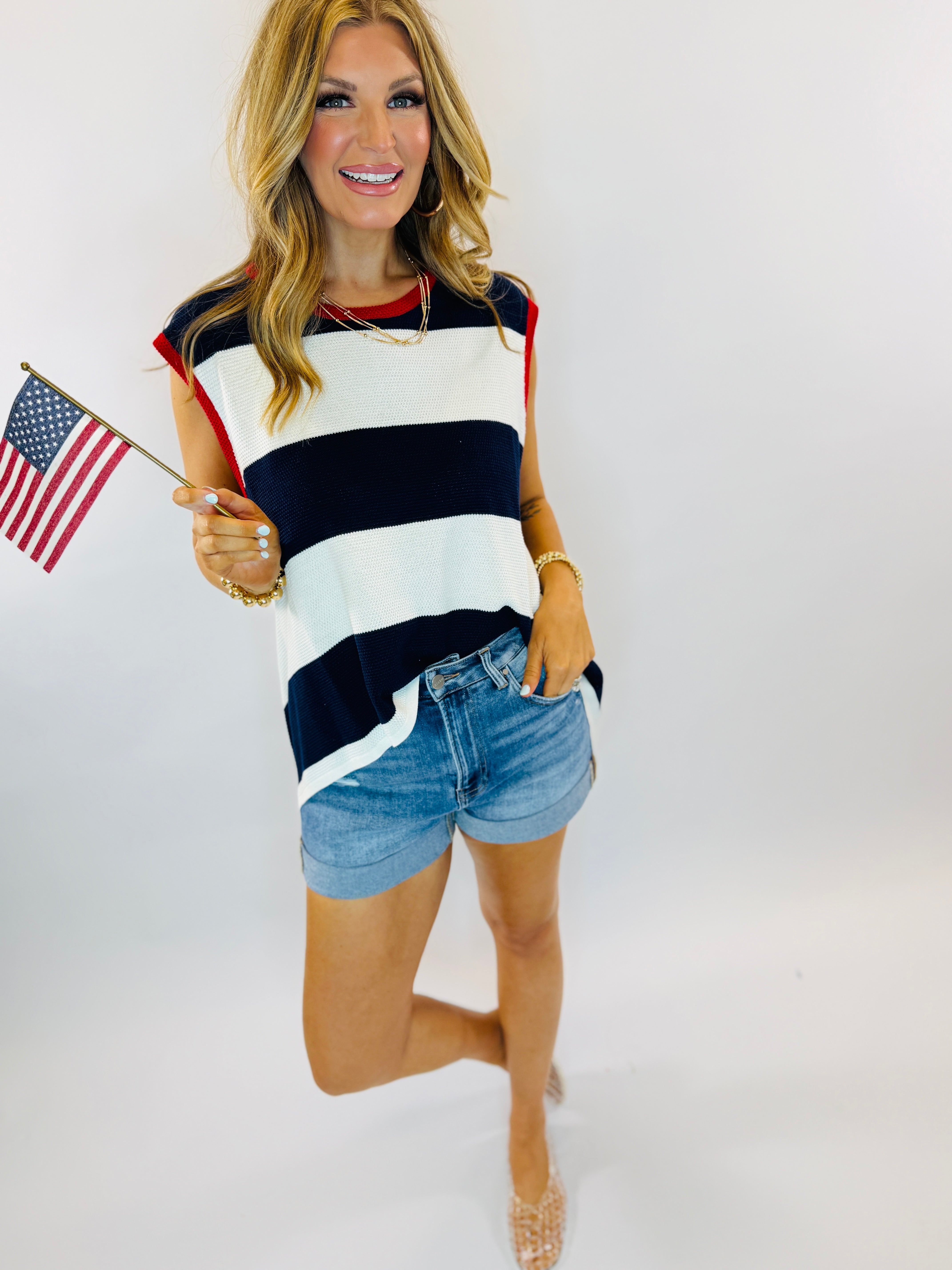 Woman wearing red, white and blue striped sleeveless tank top with denim shorts, holding small American flag