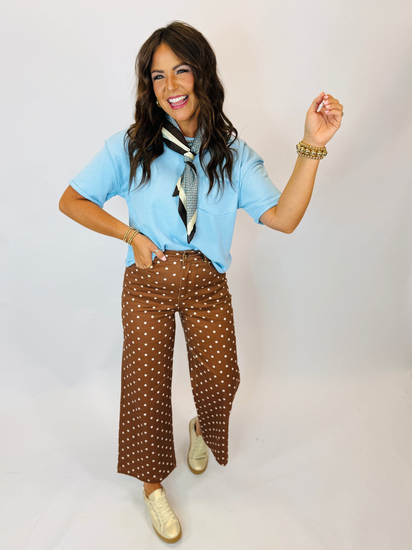 Woman wearing light blue short-sleeve Becka Top with neck scarf, paired with brown polka dot wide-leg pants.