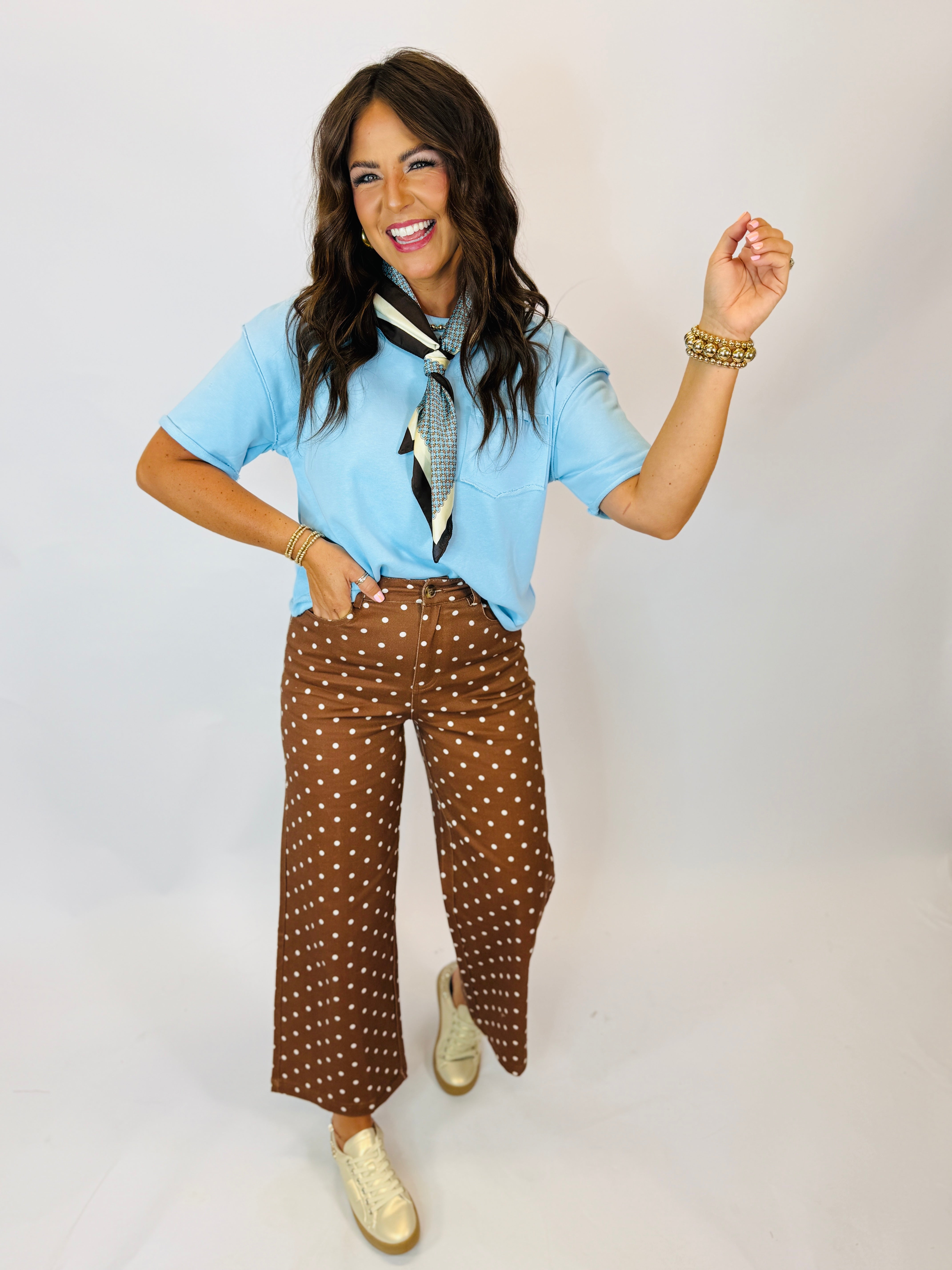 Woman wearing light blue short-sleeve Becka Top with neck scarf, paired with brown polka dot wide-leg pants.