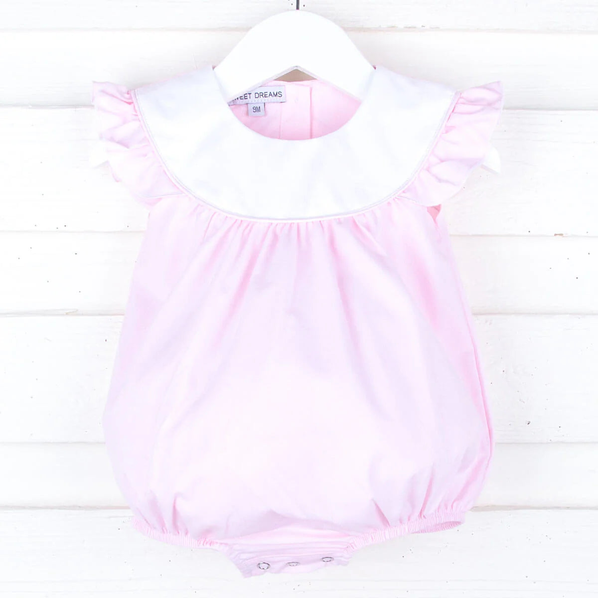 Pink baby girl bubble romper with white collar and ruffled sleeves hanging on white hanger