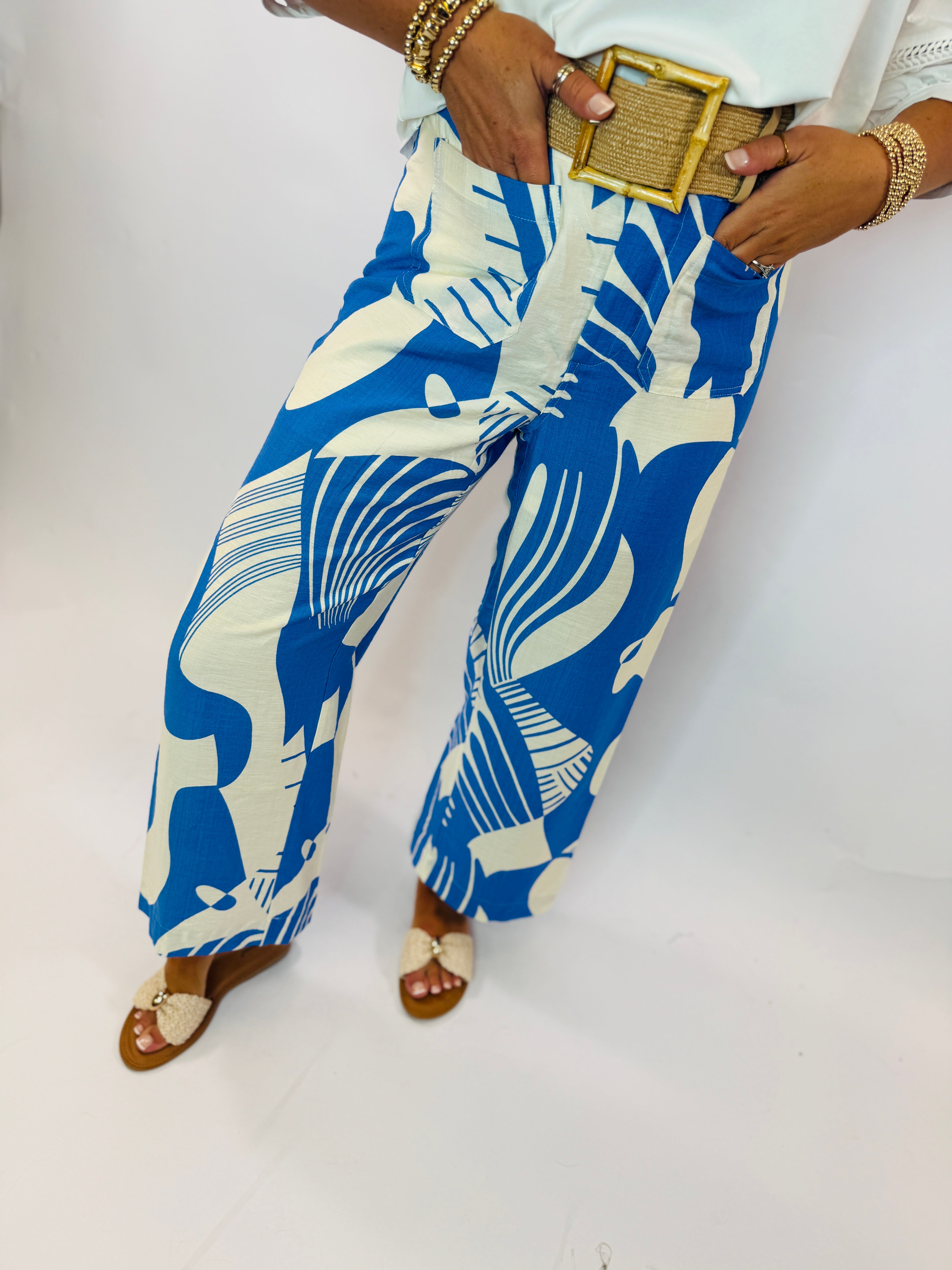 Wide-leg blue and white tropical print pants worn with gold accessories and woven sandals